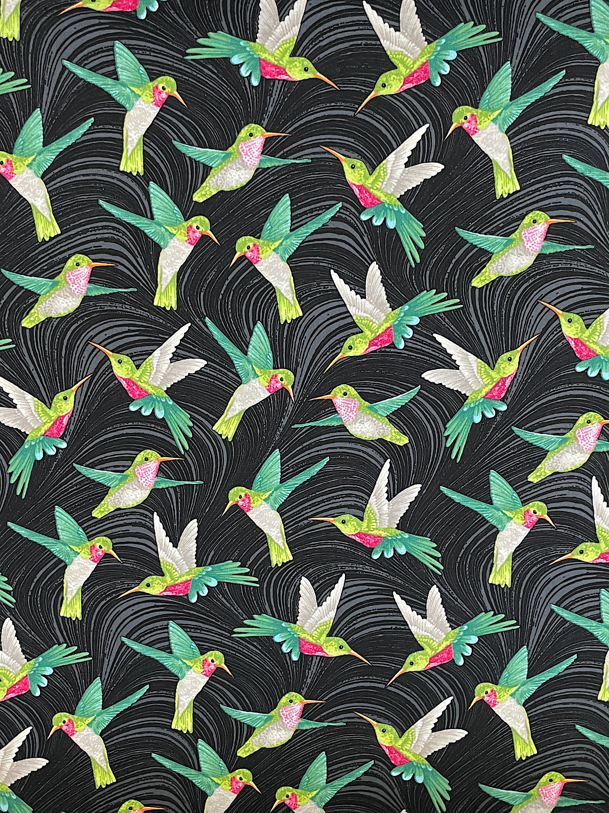 Black cotton fabric covered with hummingbirds that are green, pink and grey.