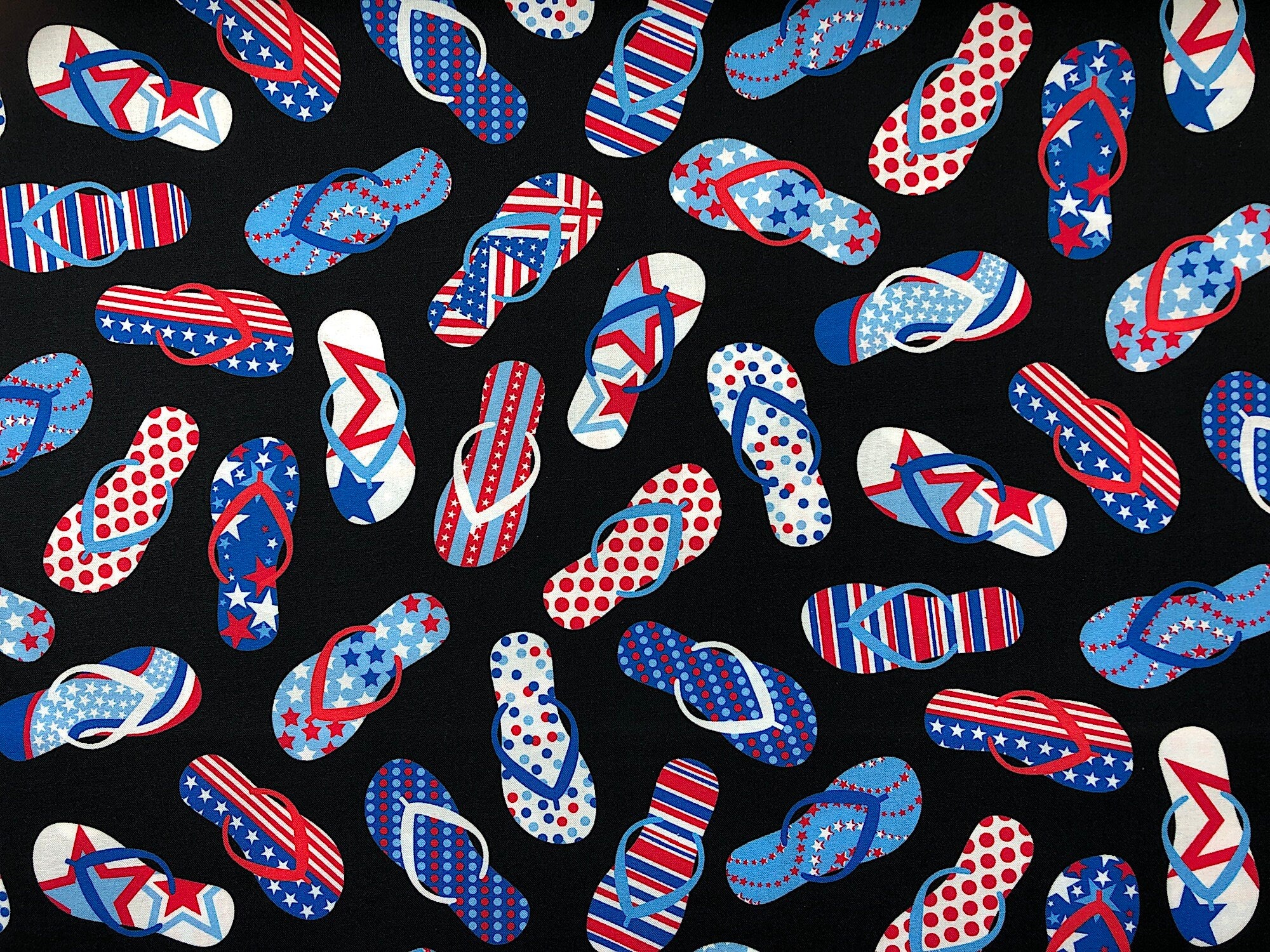Black cotton fabric covered with flip flops with different red, white and blue designs on them.