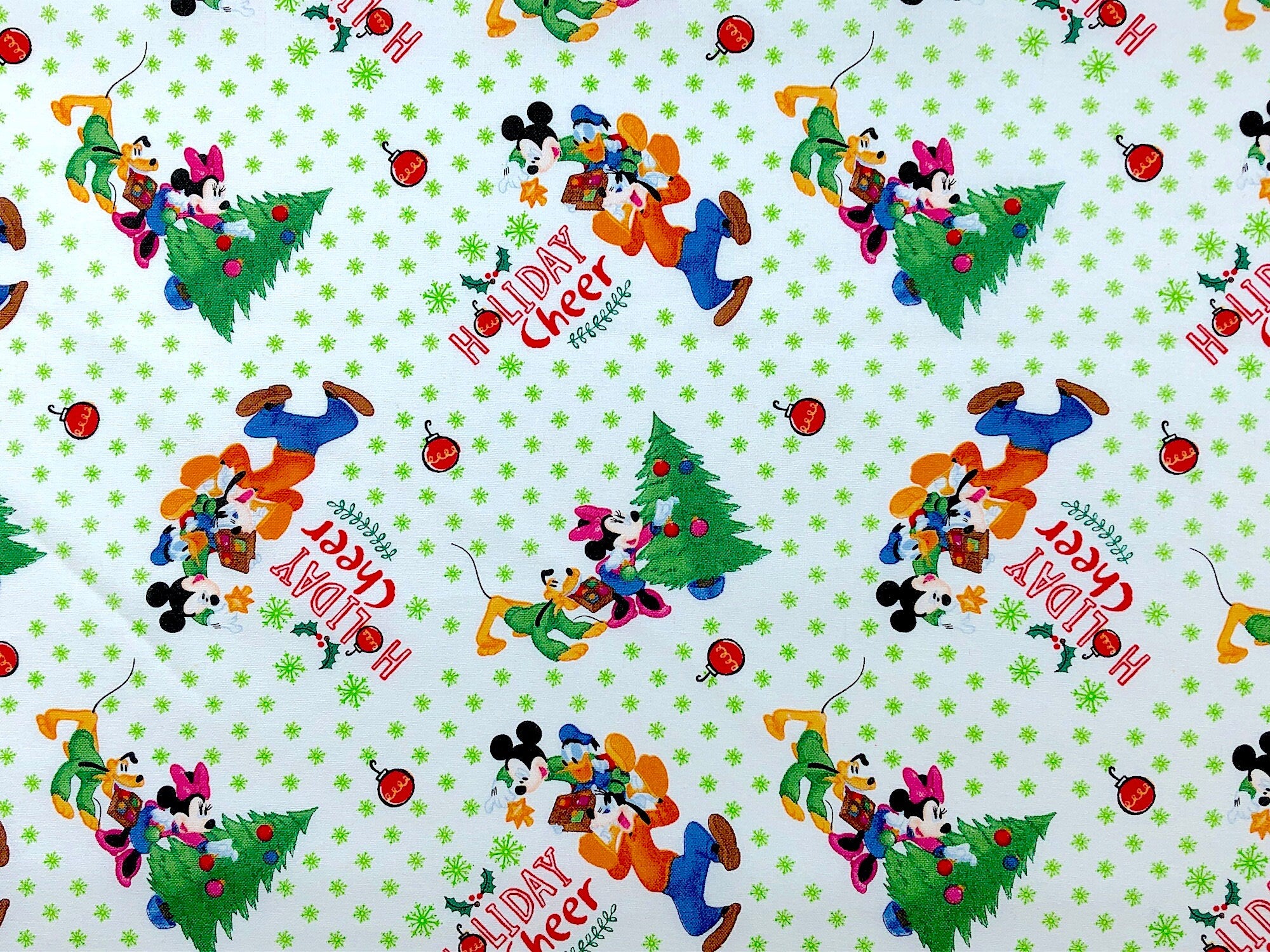 This fabric is called Mickey & Friends Trim the Tree. You will find Mickey Mouse, Minnie Mouse and Pluto trimming a Christmas Tree. Holiday Cheers is printed on the white fabric and there are single ornaments scattered about.
