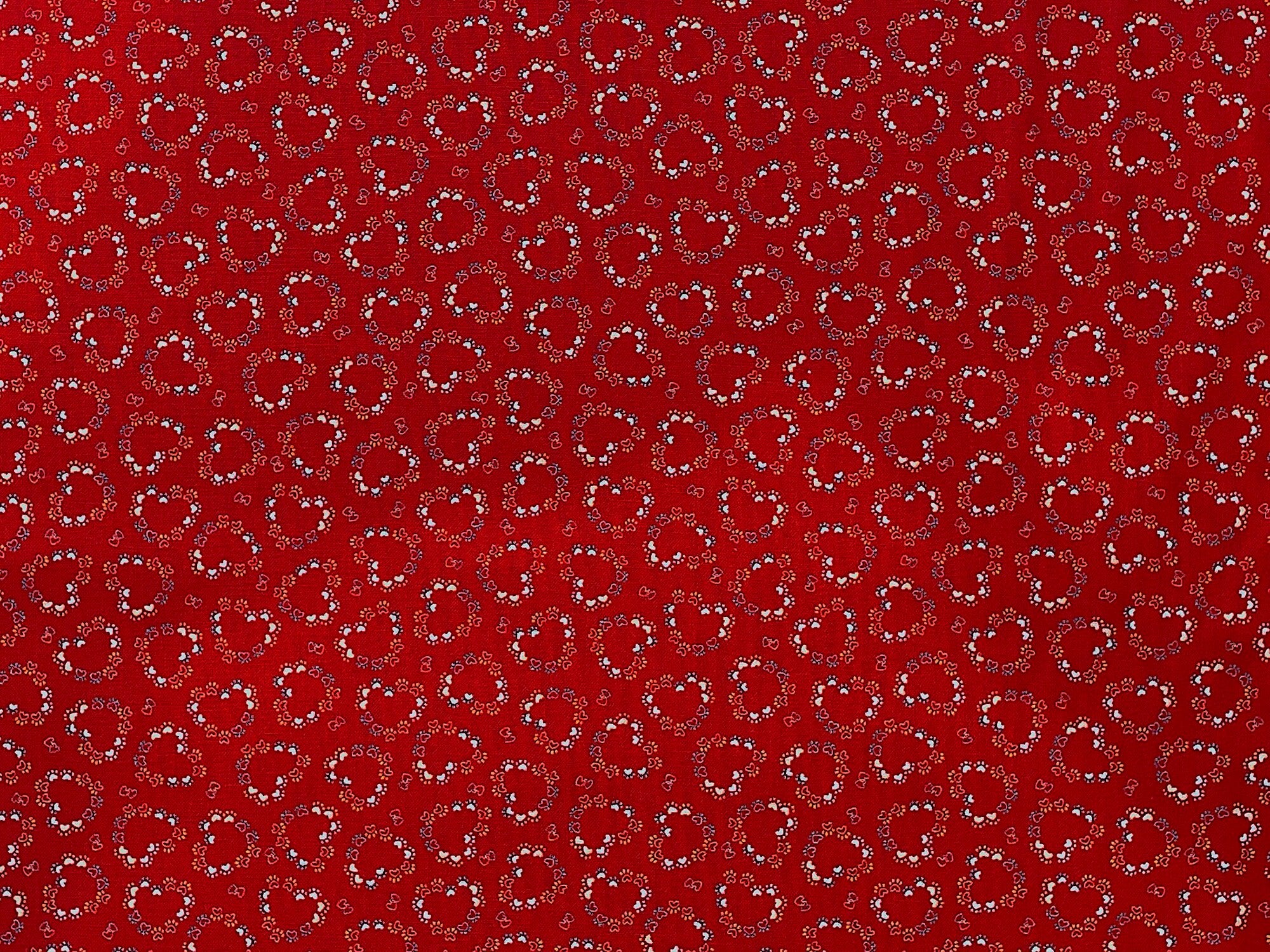 Red cotton fabric covered with paw prints and hearts.