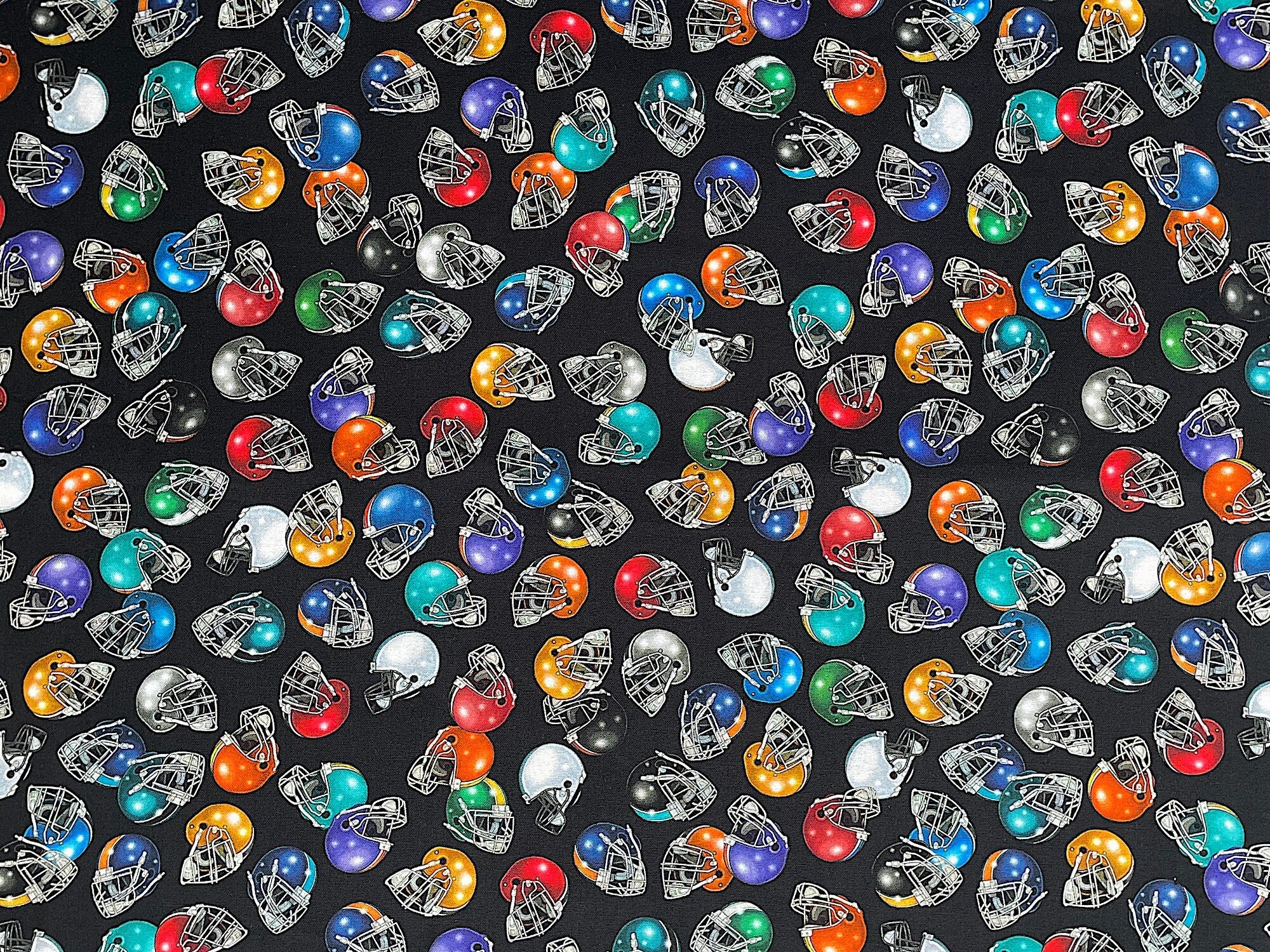 Black cotton fabric covered with white, blue, green red and yellow football helmets.
