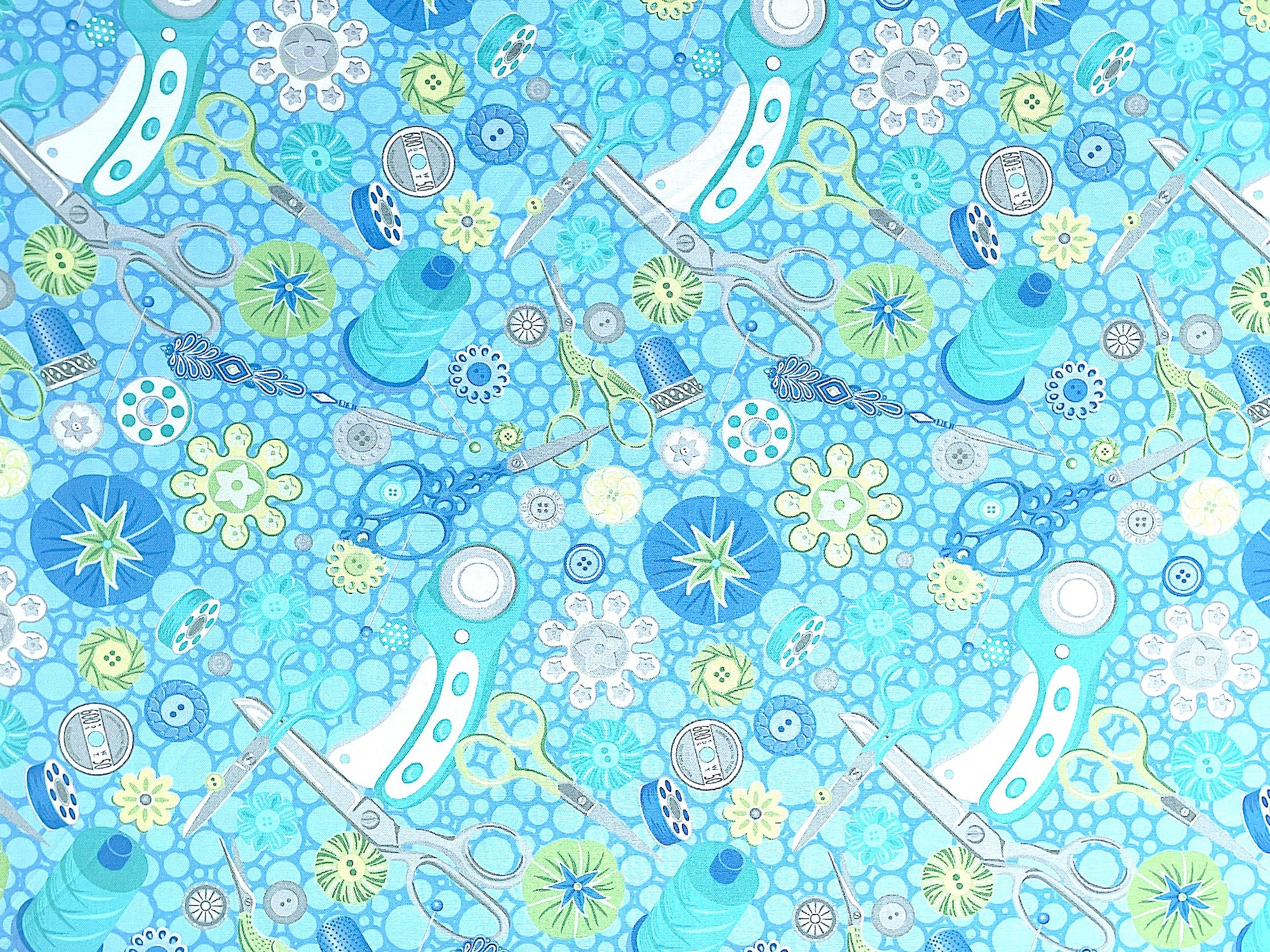 Blue cotton fabric covered with sewing scissors, rotary cutters, thread and other sewing tools.