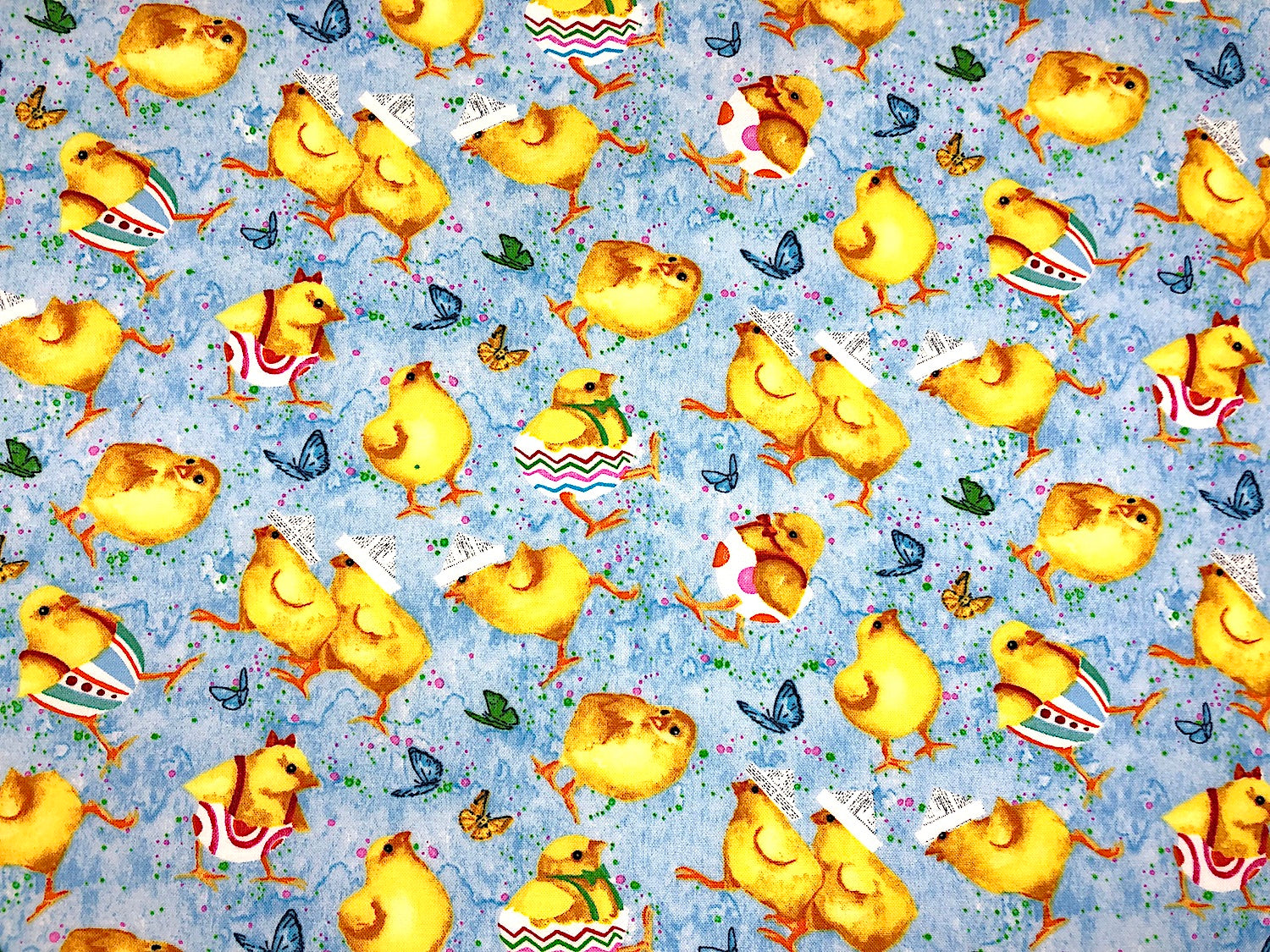 Blue cotton fabric covered with Easter Chicks, some of the chicks are coming out of decorated Easter eggs and others are wearing hats.