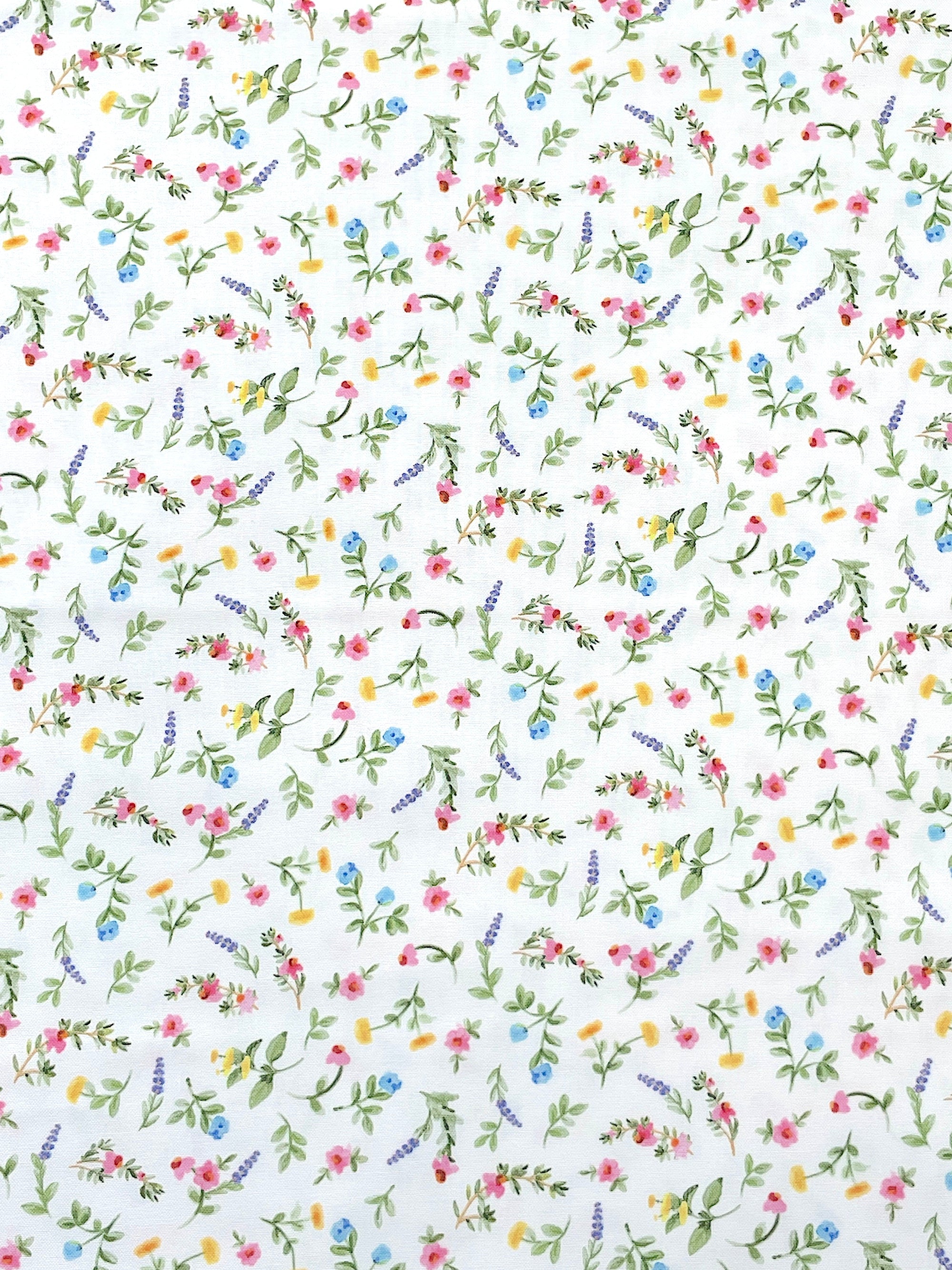 White cotton fabric covered with small pink, blue and yellow fabrics and green stems and leaves.