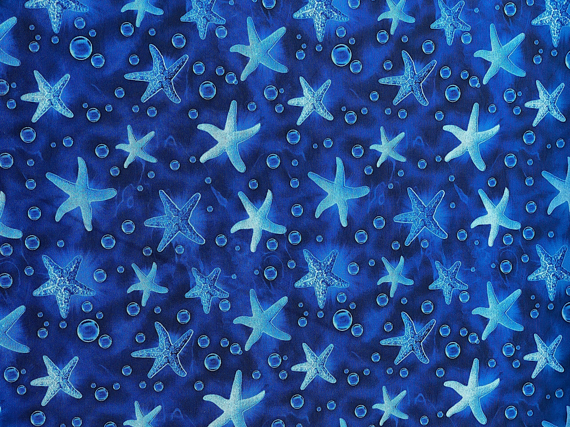 This blue cotton fabric is covered with starfish and bubbles. This fabric is part of the Ocean Story collection.