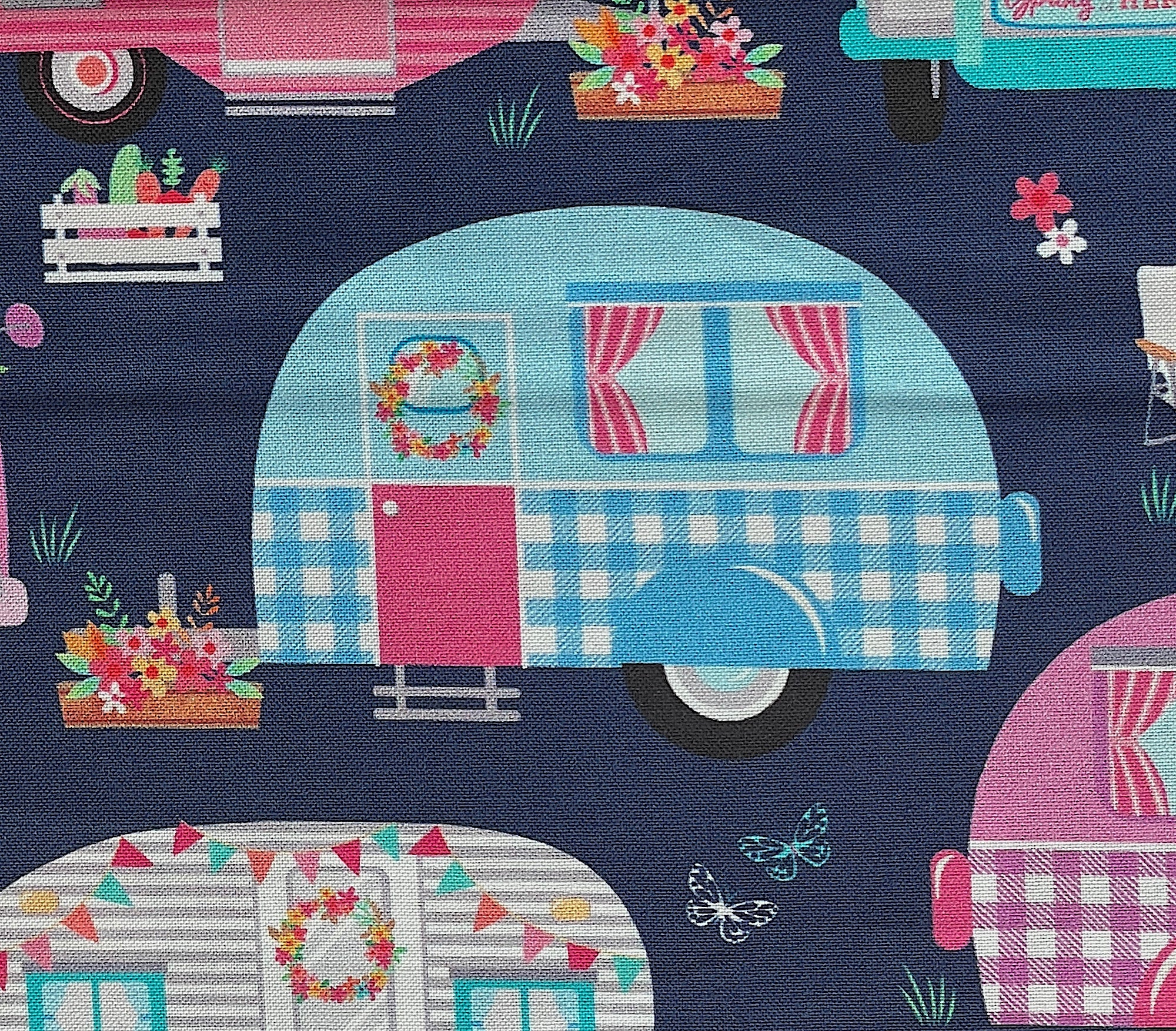 Close up of a blue, white and pink travel trailer with a box of flowers outside of it.