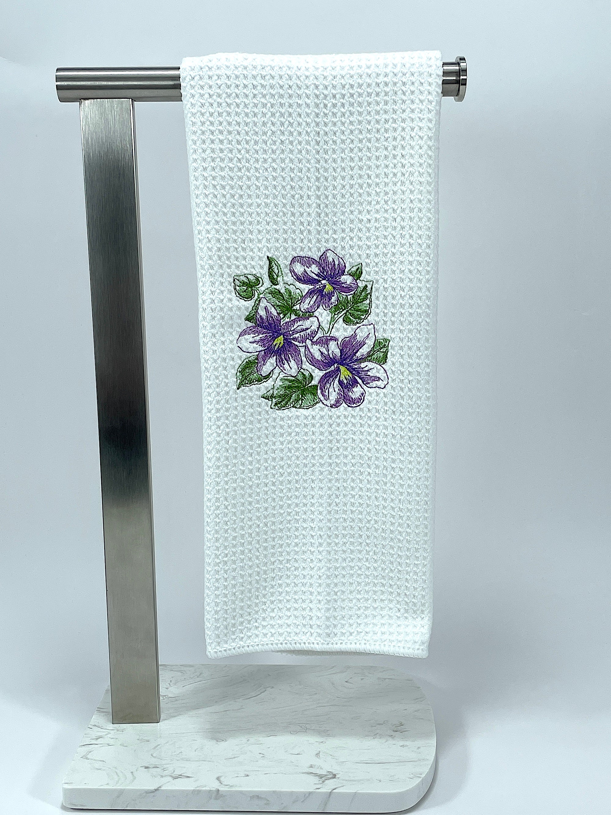 White towel with purple floral design on a metal stand against a white background