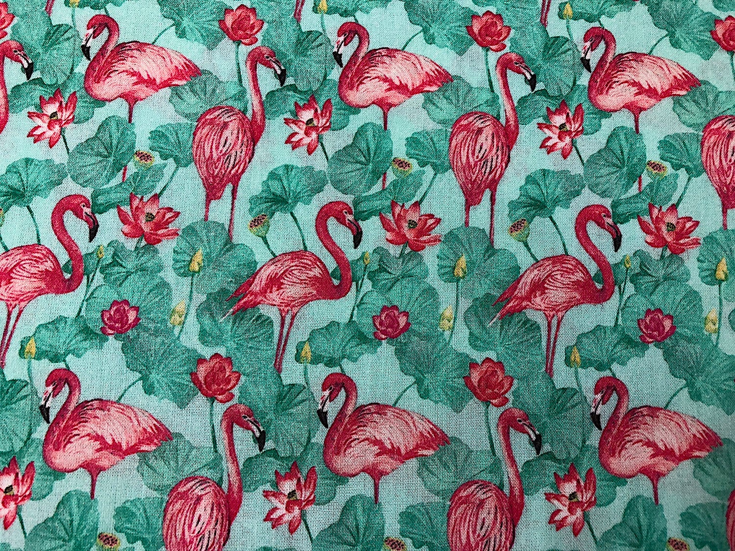 Cotton fabric covered with pink flamingoes and green leaves.