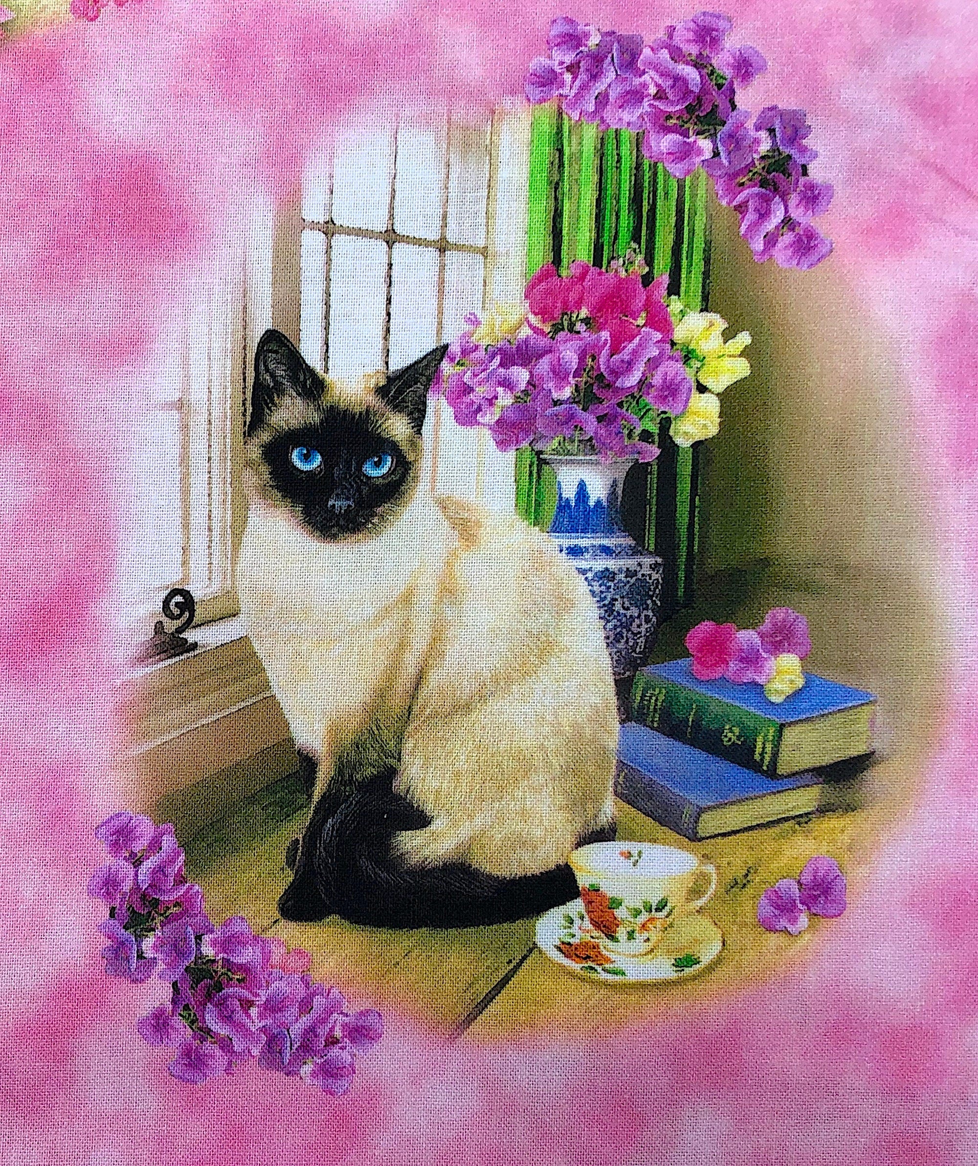 Close up of a Siamese cat sitting in front of f window by a vase of flowers.