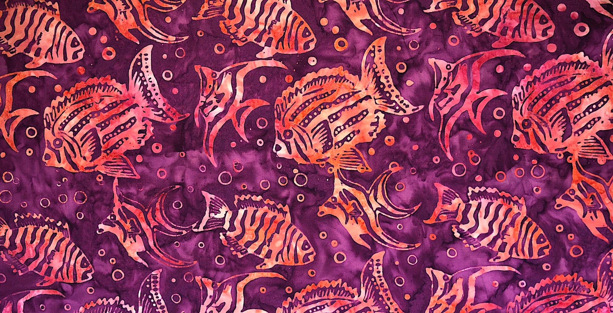 This fabric is called Batik Down under and has shades of red and orange fish on a background that has shades of burgundy/reds.
