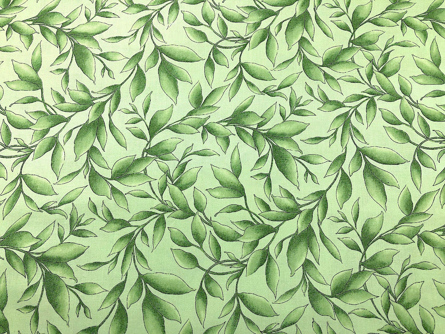 This light green cotton fabric is covered with dark and light green leaves.