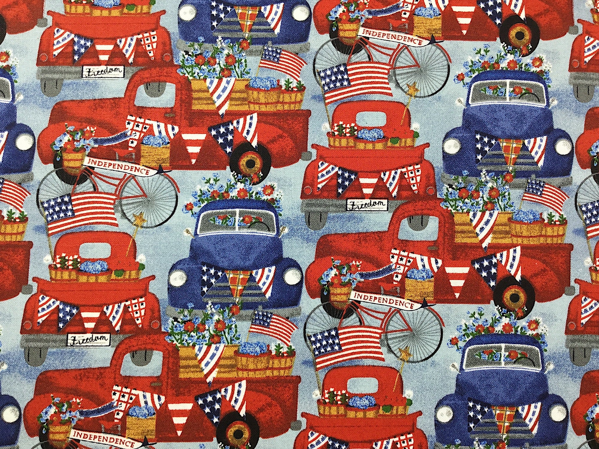 This fabric is called American Spirit American Trucks and has red and blue trucks on a blue background. The trucks are filled with Red, White and Blue Flowers and are draped in patriotic flags.
