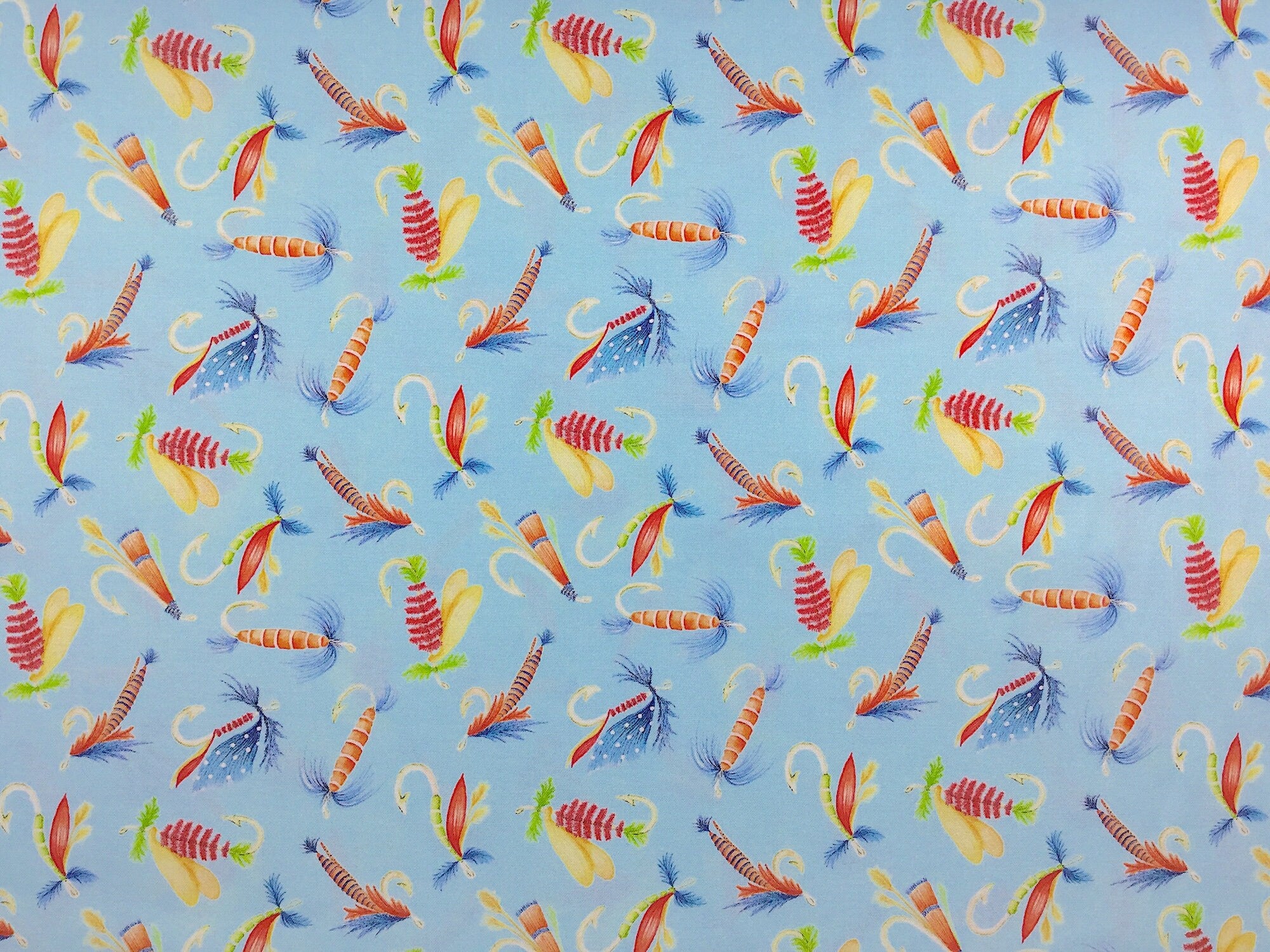 This fabric is covered with fishing lures on a light blue background.