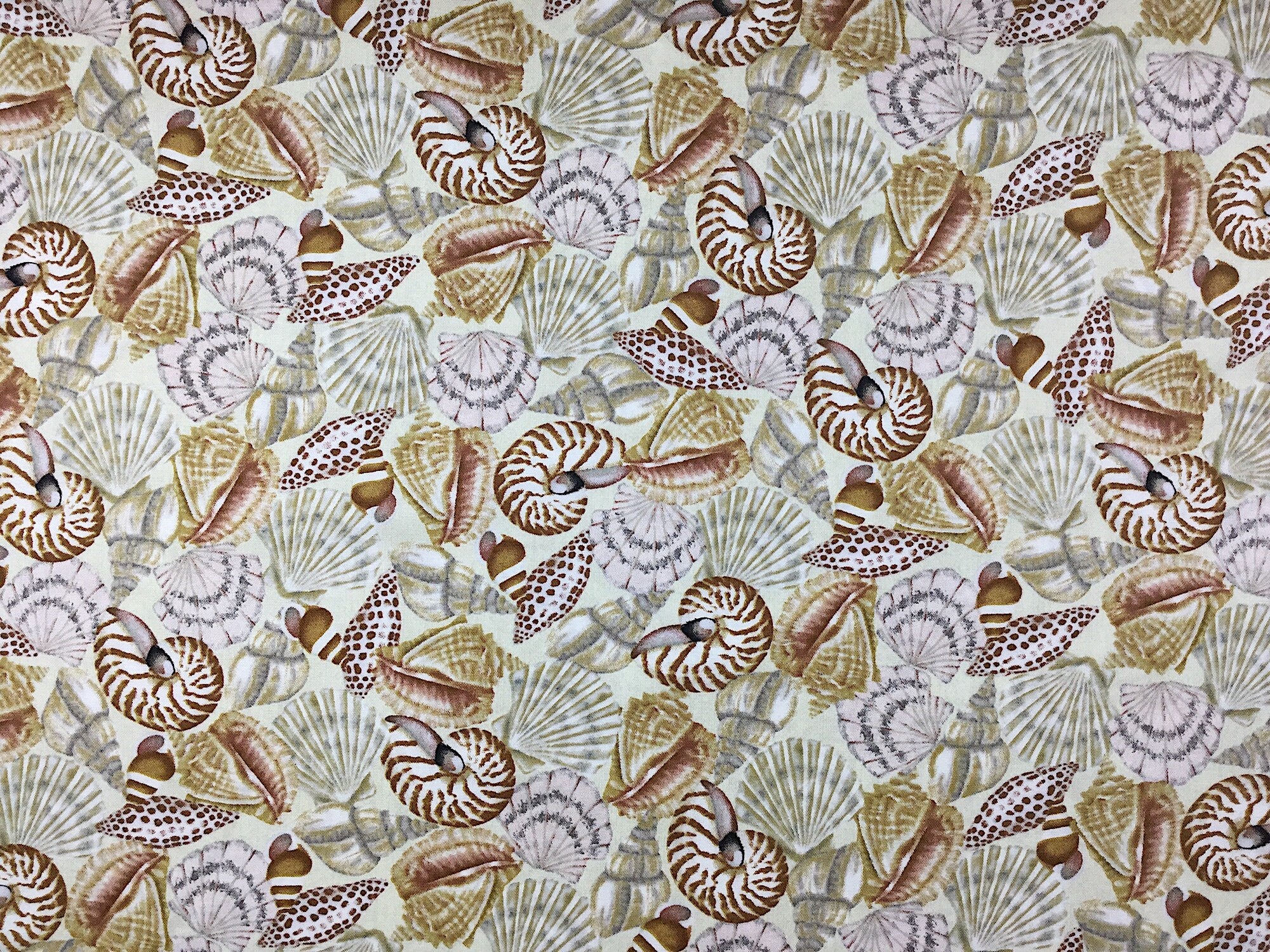 This fabric is called Seaside Dreams and is covered with seashells in shades of brown, tan, and grey on a off white background.