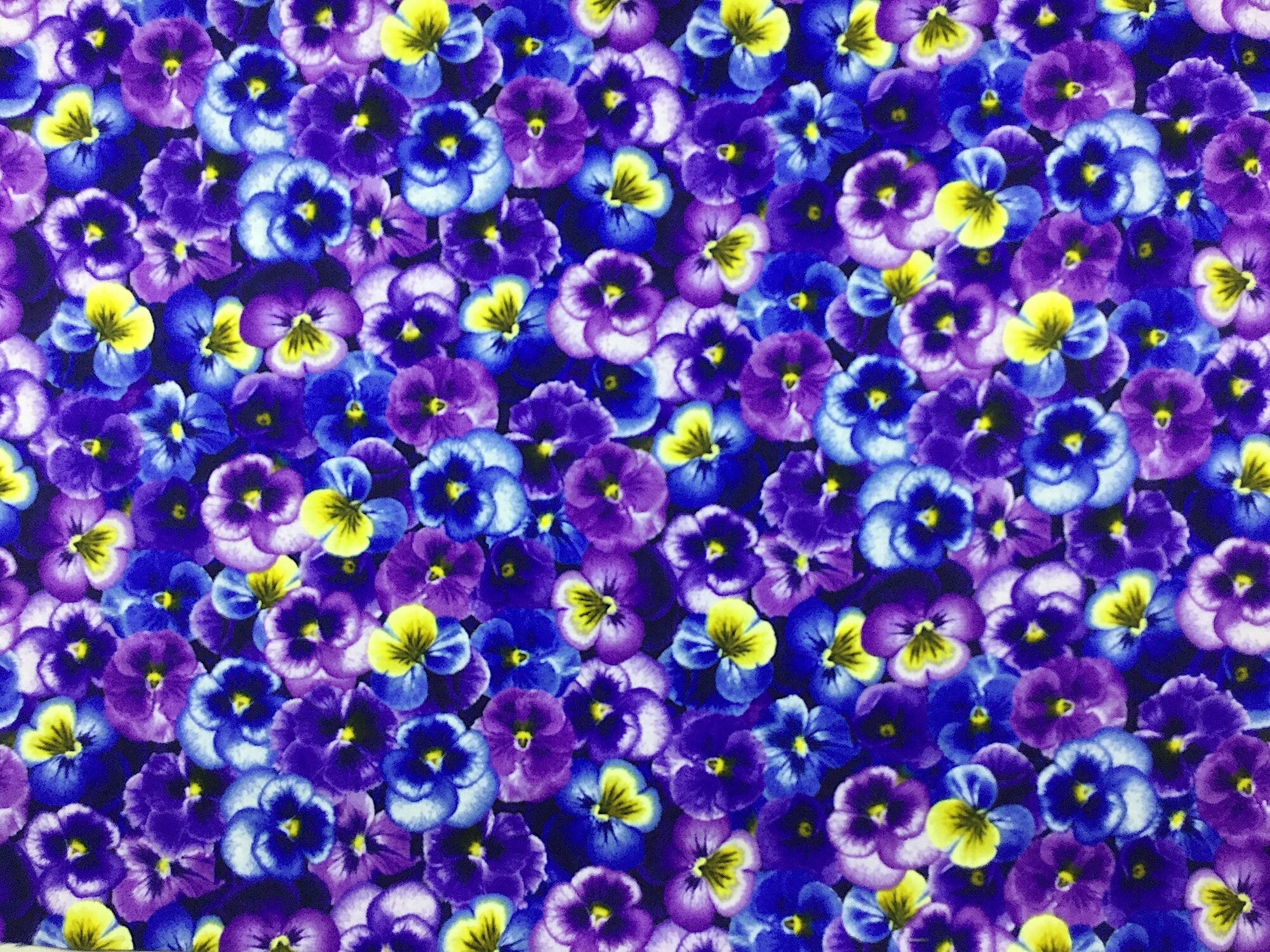 This fabric is covered with purple and blue pansies. The pansies are packed closely together to make them a bed of pansies.