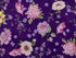 This fabric is covered with a variety of flowers in pinks, purples, and white on a purple background.