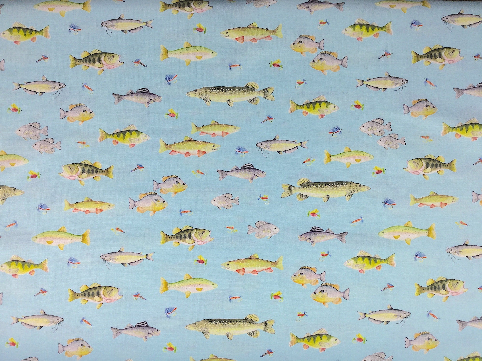 This fabric is covered with fish and fishing flies on a light blue background.