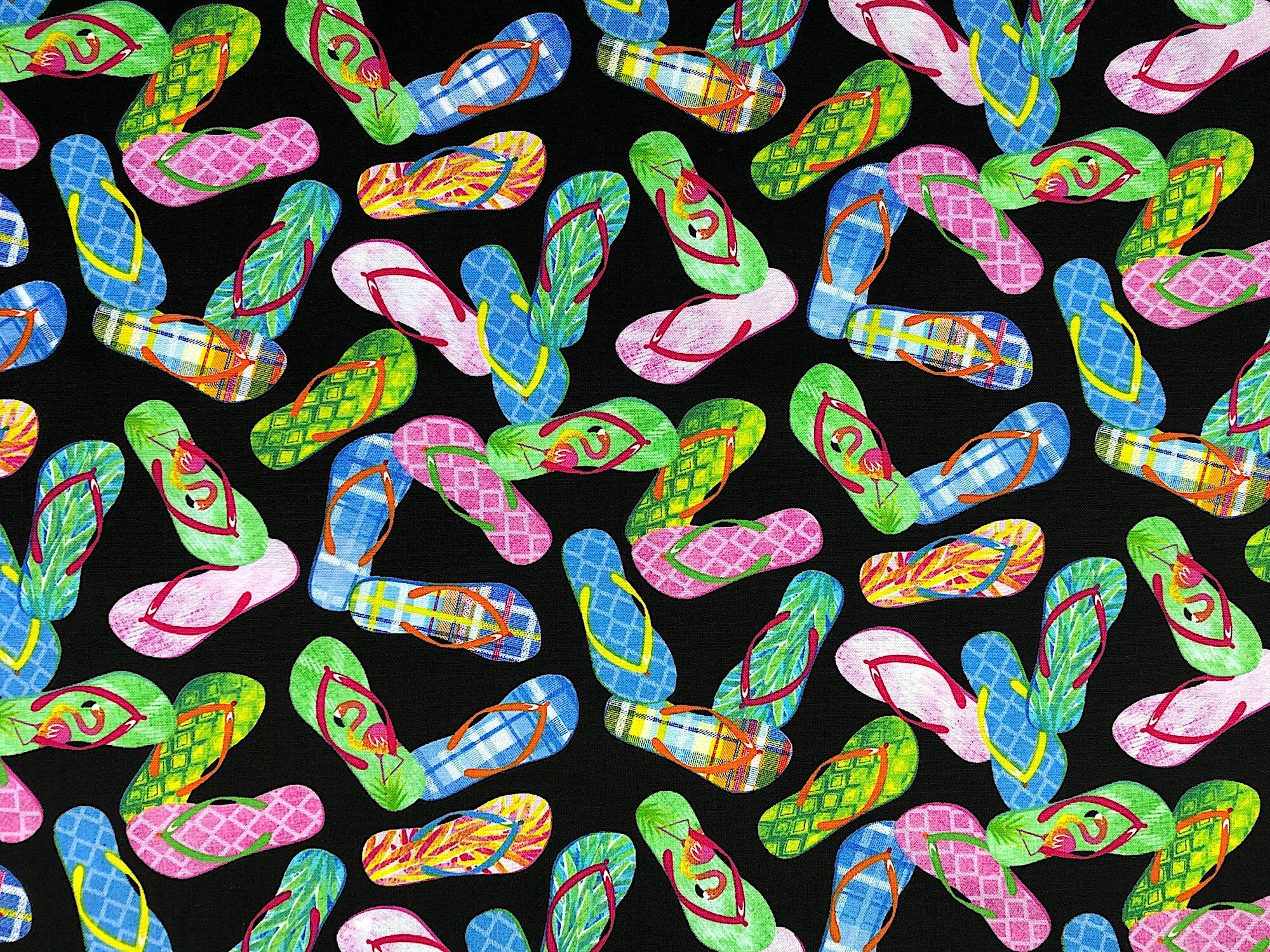 This black fabric is covered with flip flops of multiple colors. The flip flops are placed randomly throughout the pattern
