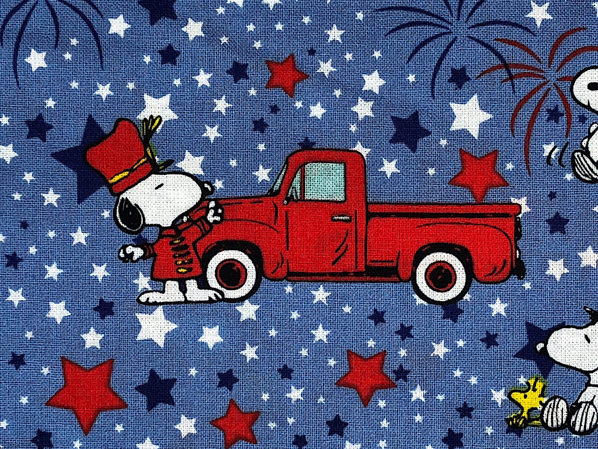 Close up of Snoopy wearing a red outfit standing next to a red truck.