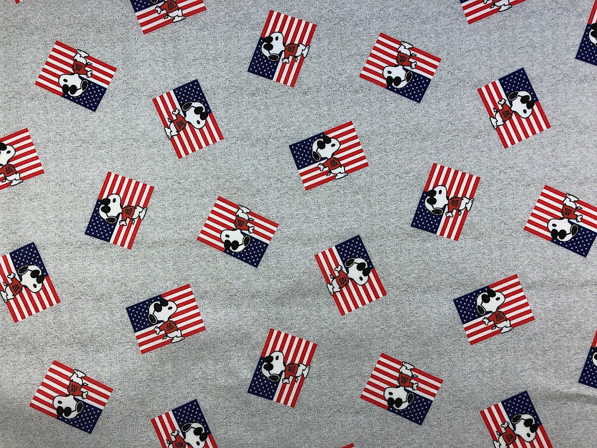 This gray fabric is covered with Snoopy standing in front of the US Flag.