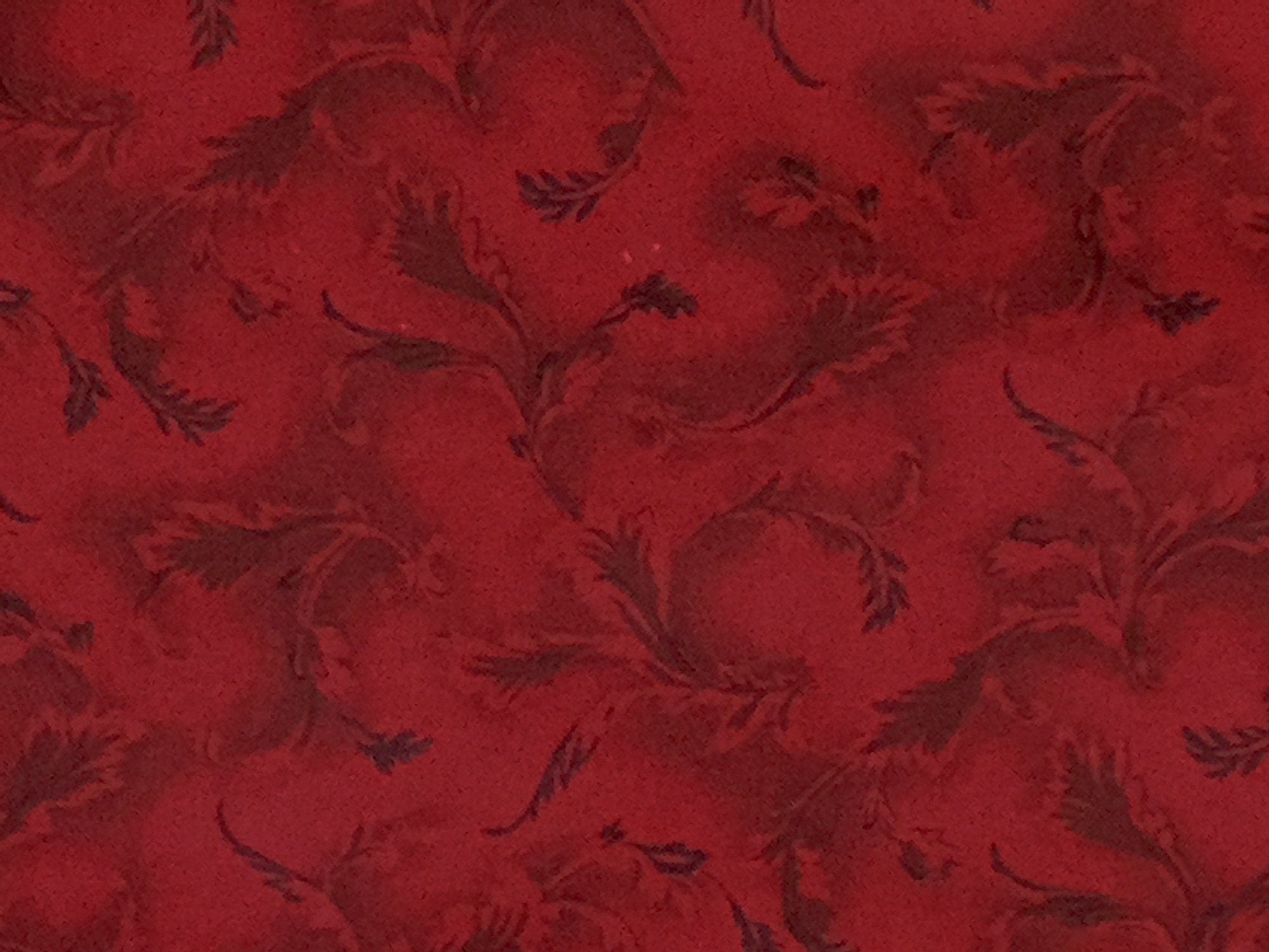 Close up of red cotton fabric covered with leaves.