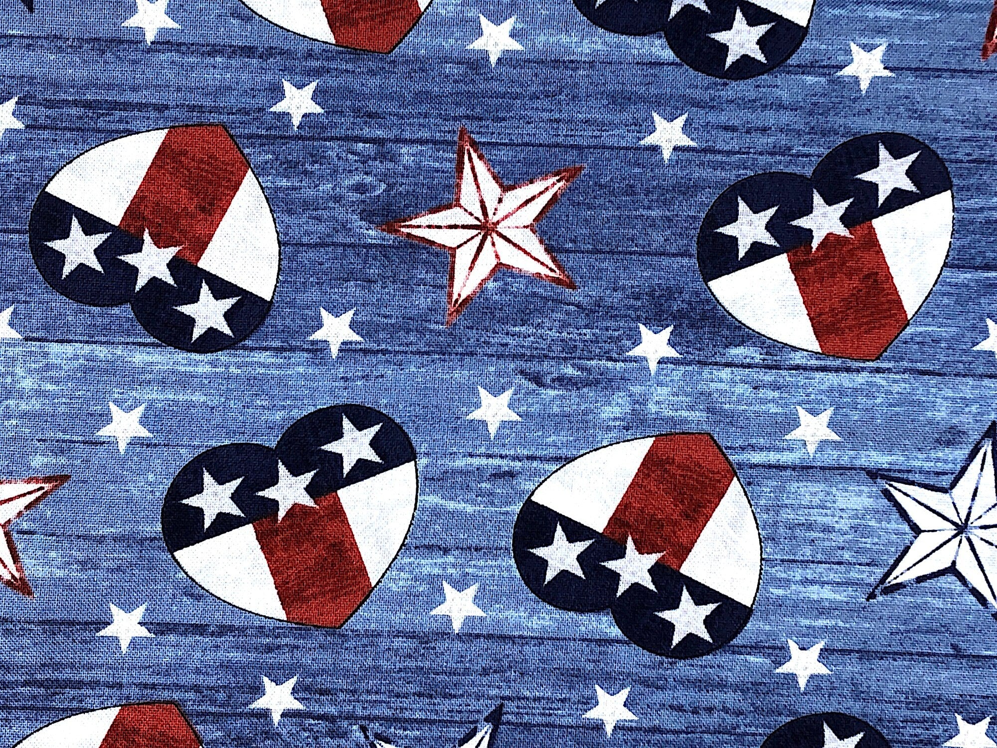 Close up of red, white and blue hearts and stars on a blue woodgrain background.