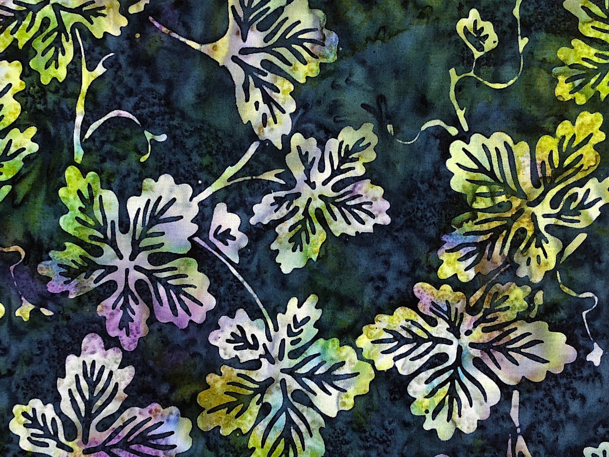 Close up of leaves that are shades of white, blue and yellow on a blue batik background.