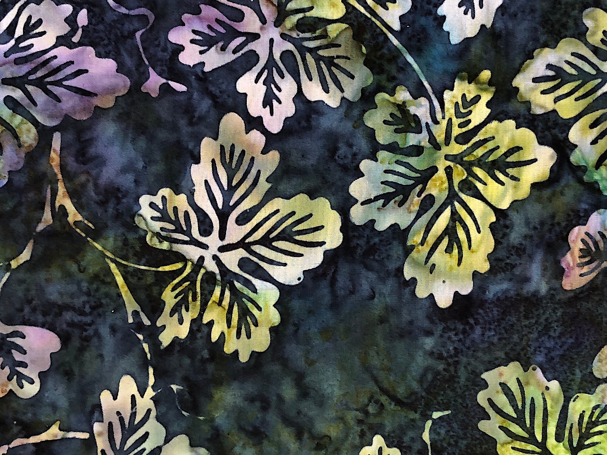 Close up of leaves that are shades of white, blue and yellow on a blue batik background.