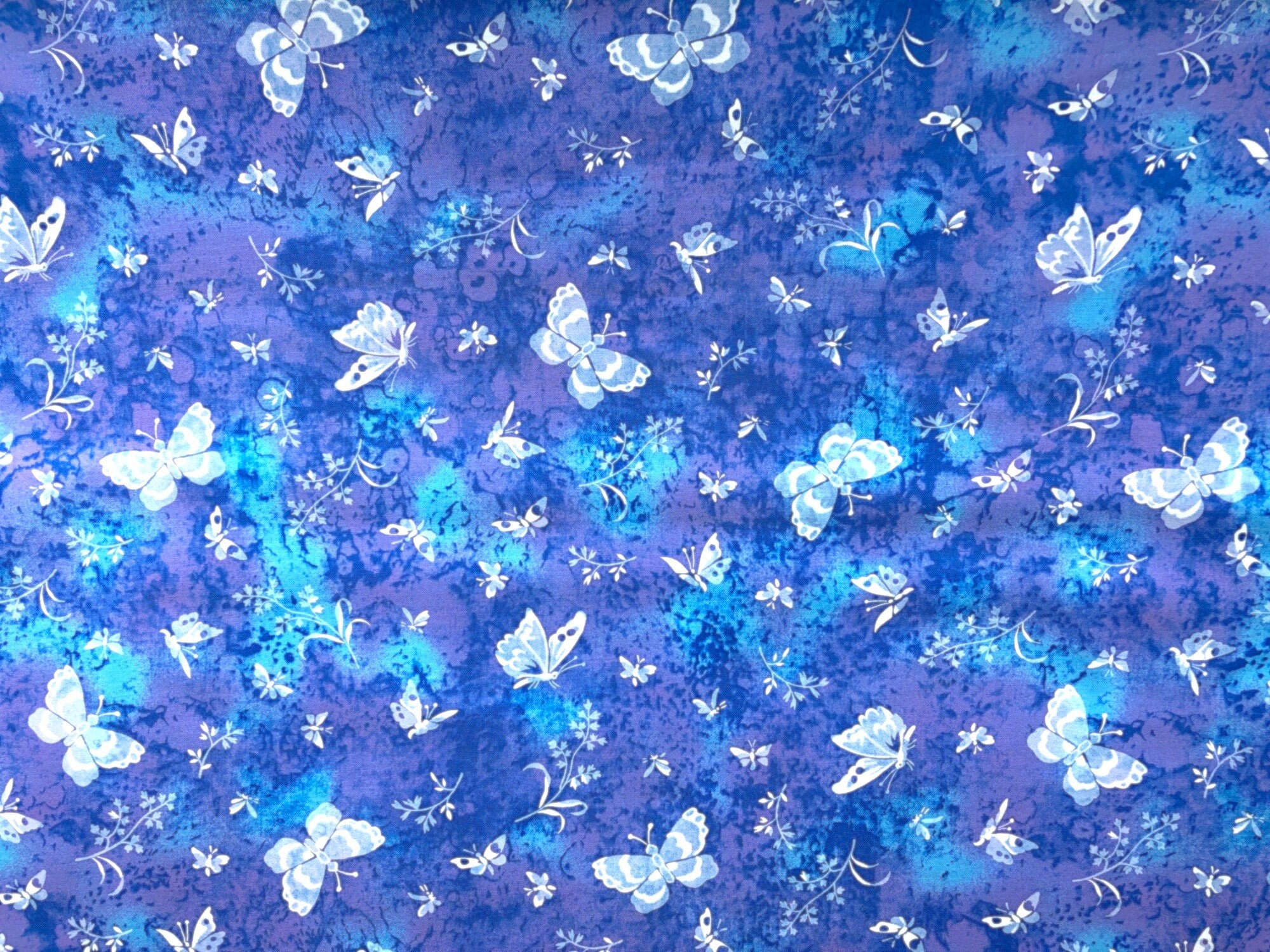 This fabric is covered with different sized white butterflies. The background is a mixture of various shades of blue and lavender.