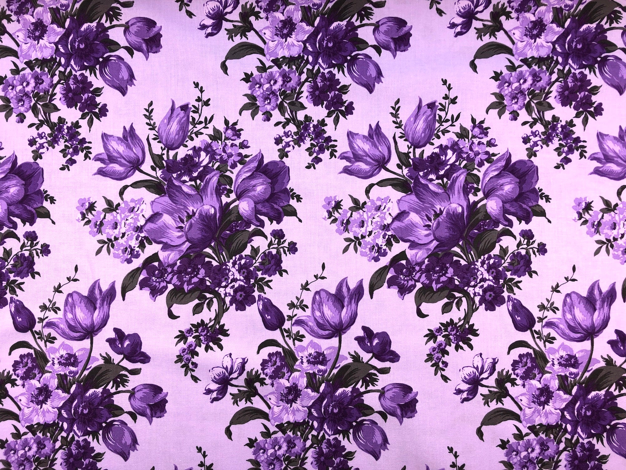 This fabric is a part of the Elegant Blooms collection and has purple and lavender flowers on a lavender background