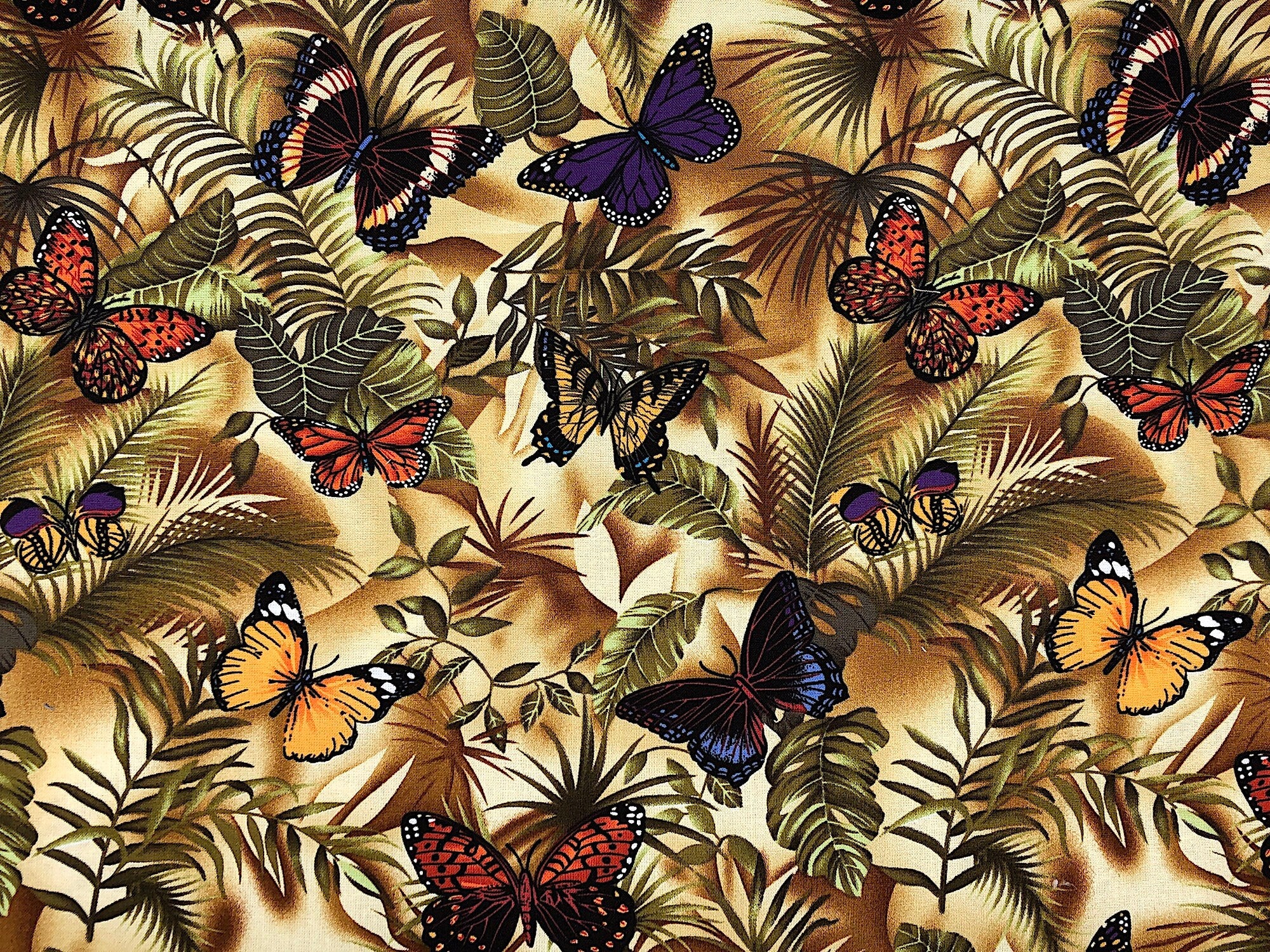 This fabric is covered with butterflies and leaves. The butterflies are shades of orange, yellow, cream and purple.