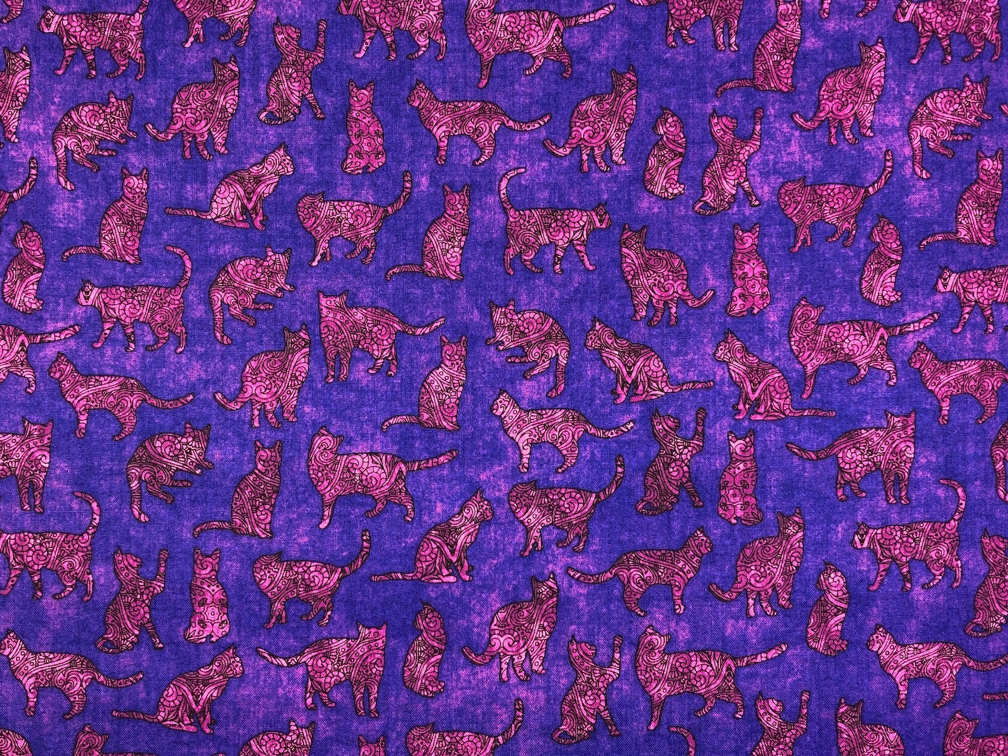 This purple fabric is covered with pink cat silhouettes. The Silhouettes have various scroll designs in them.