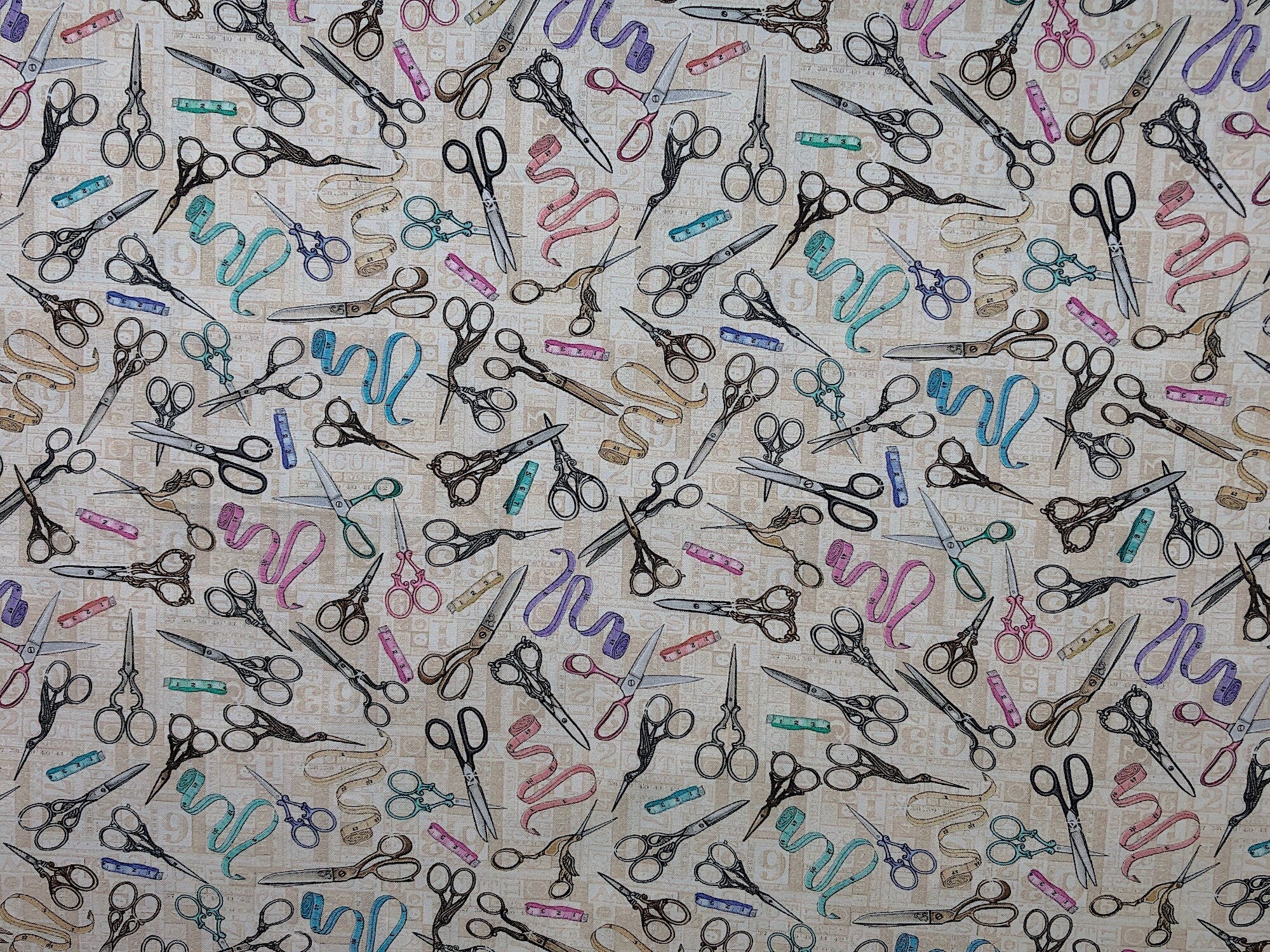 This fabric is part of the Tailor Made collection. This taupe cotton fabric is covered with scissors and tape measures. The scissors are in different styles and colors such as silver, gold, blue and pink. The tape measures are either pink, yellow, blue, green, lavender or cream. 