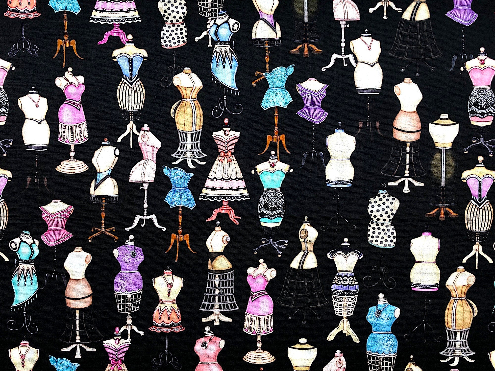 This fabric is part of the Tailor Made collection. This black cotton fabric is covered with dress forms. The dress forms have various styles of dresses on them that are pink, green, blue and lavender.