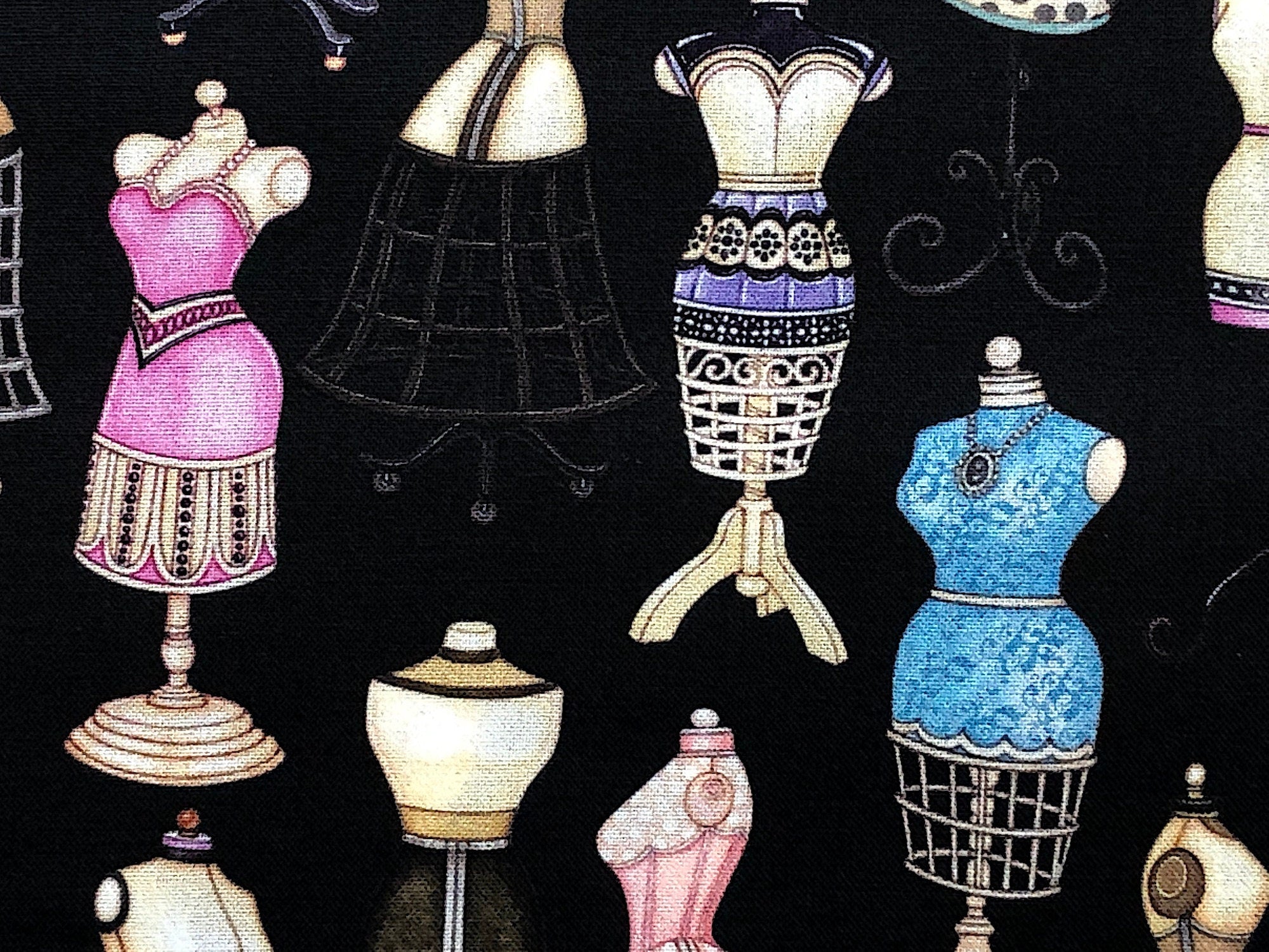 This fabric is part of the Tailor Made collection. This black cotton fabric is covered with dress forms. The dress forms have various styles of dresses on them that are pink, green, blue and lavender.