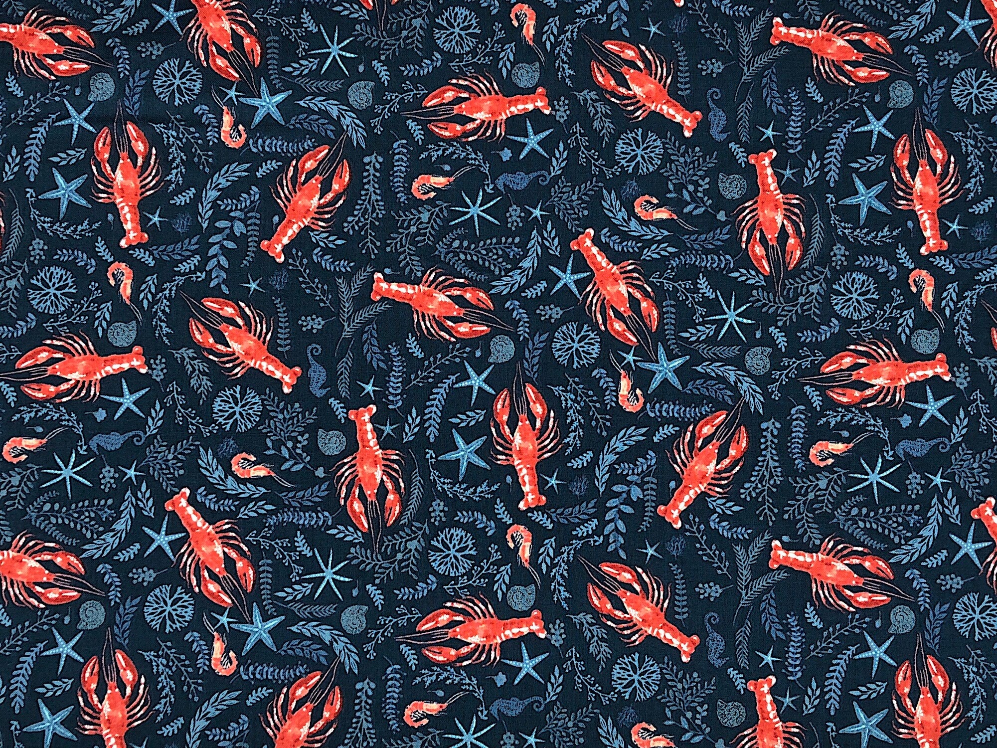 This fabric is called Oxford Lobster. This blue fabric is covered with red lobsters and plants.
