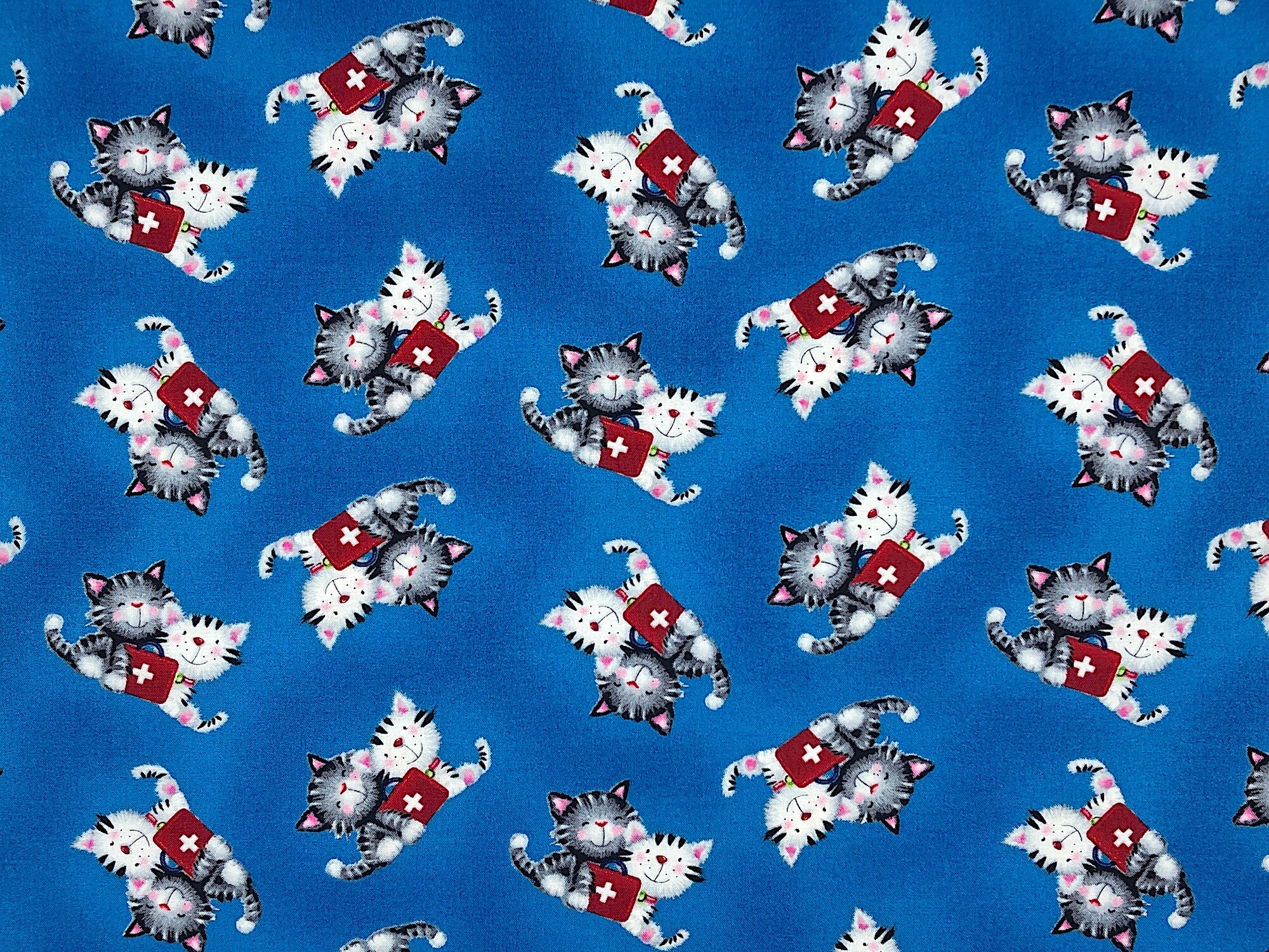 This fabric is part of the big hugs collection. The blue fabric is covered with grey and white cats. There is a first aid kit sitting in front of the cats.