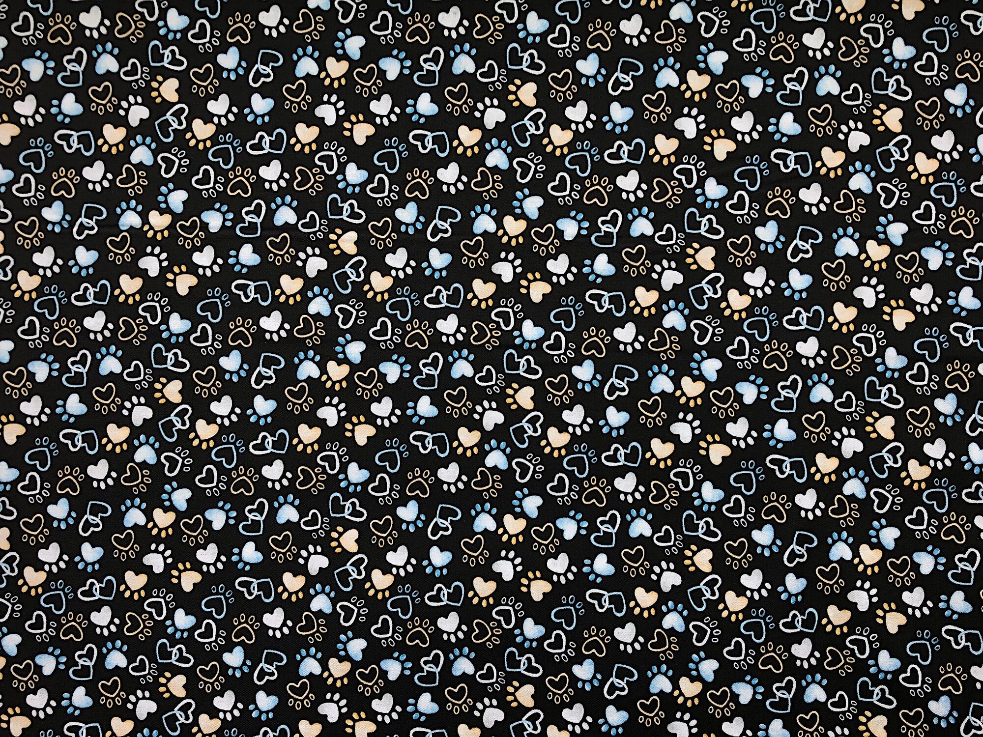 This black fabric is covered with paw prints and hearts. This fabric is part of the Think Pawsitive collection designed by Andi Metz