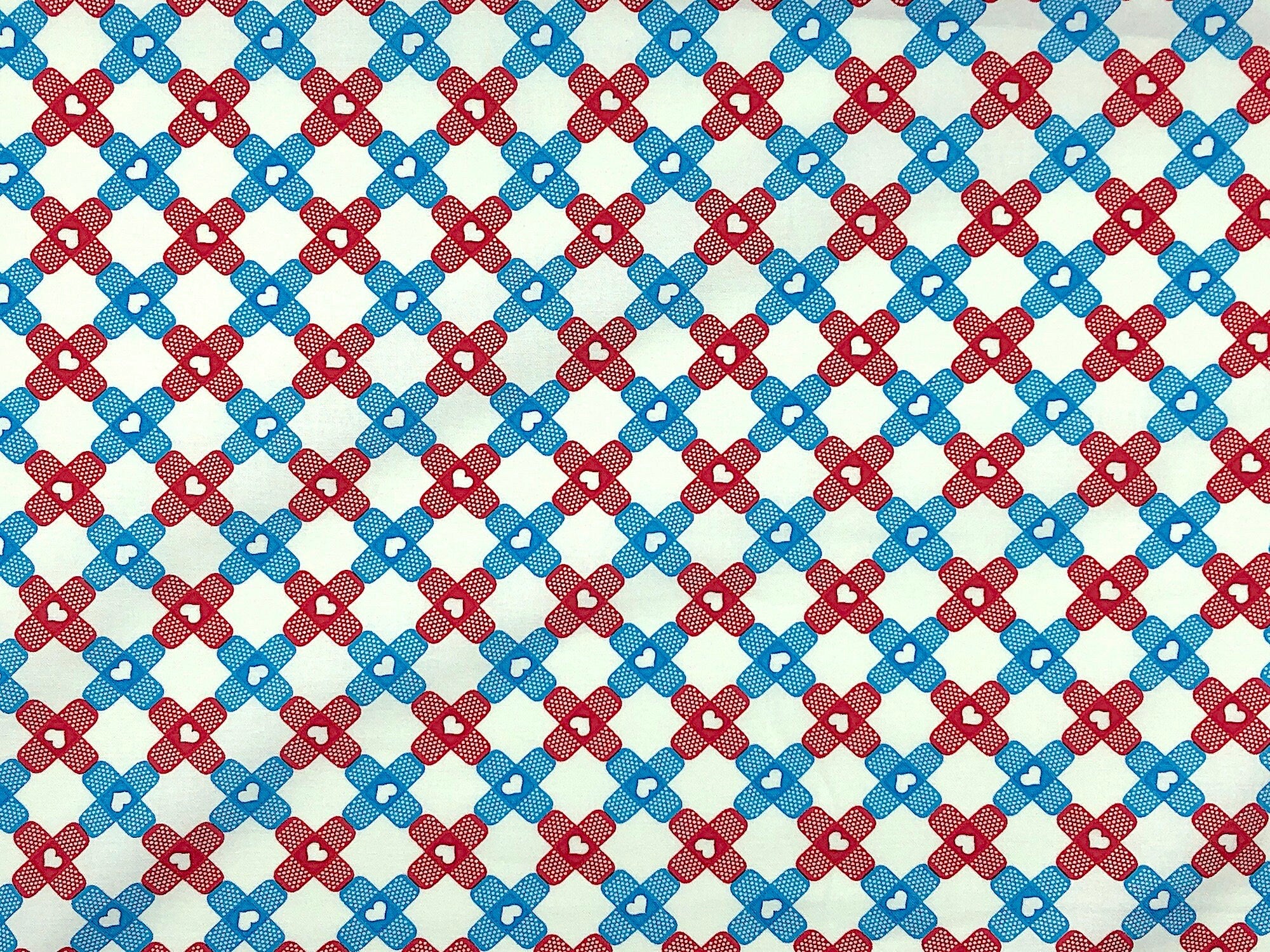 This fabric is part of the big hugs collection. The white fabric is covered with blue and red band aids. The band aids are arranged in a checkered pattern and have hearts in the middle of them.
