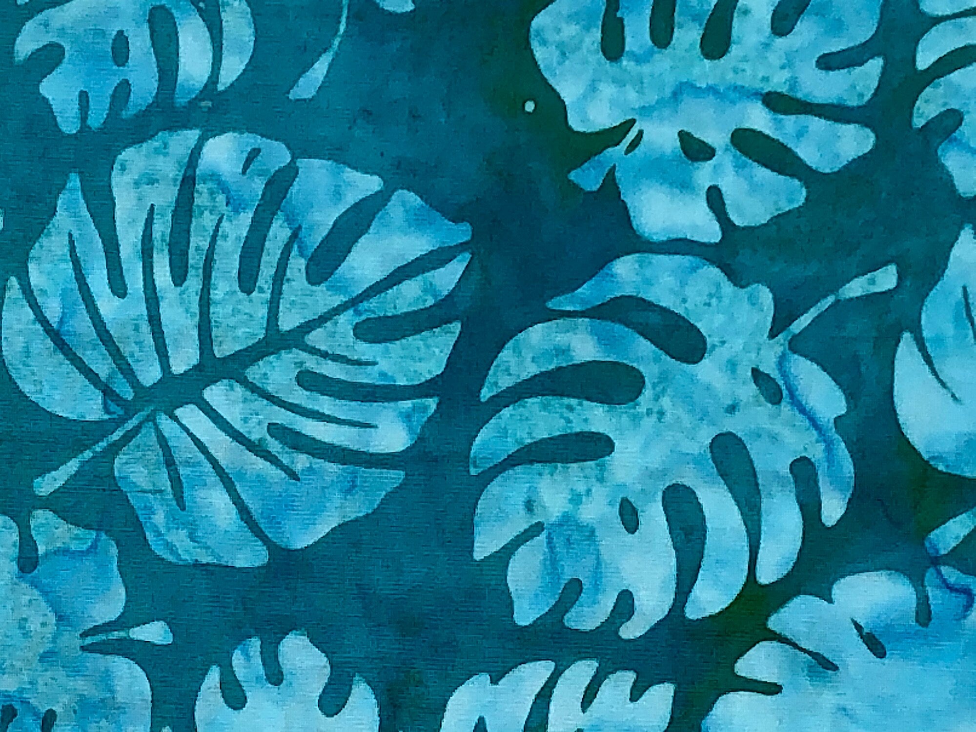 Turquoise blue batik fabric covered with leaves.