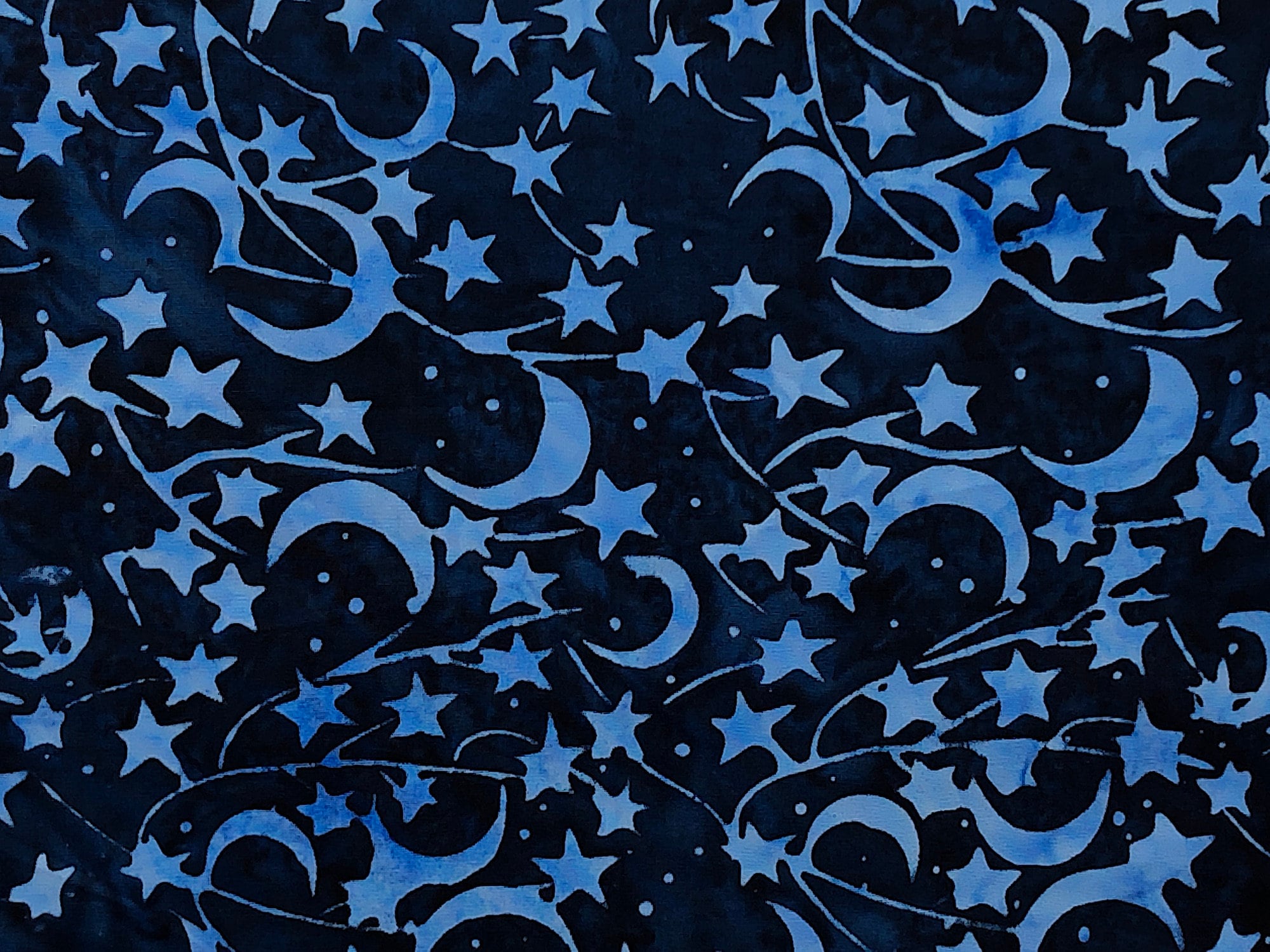 Close up of blue moons and stars on a dark blue batik cotton fabric.