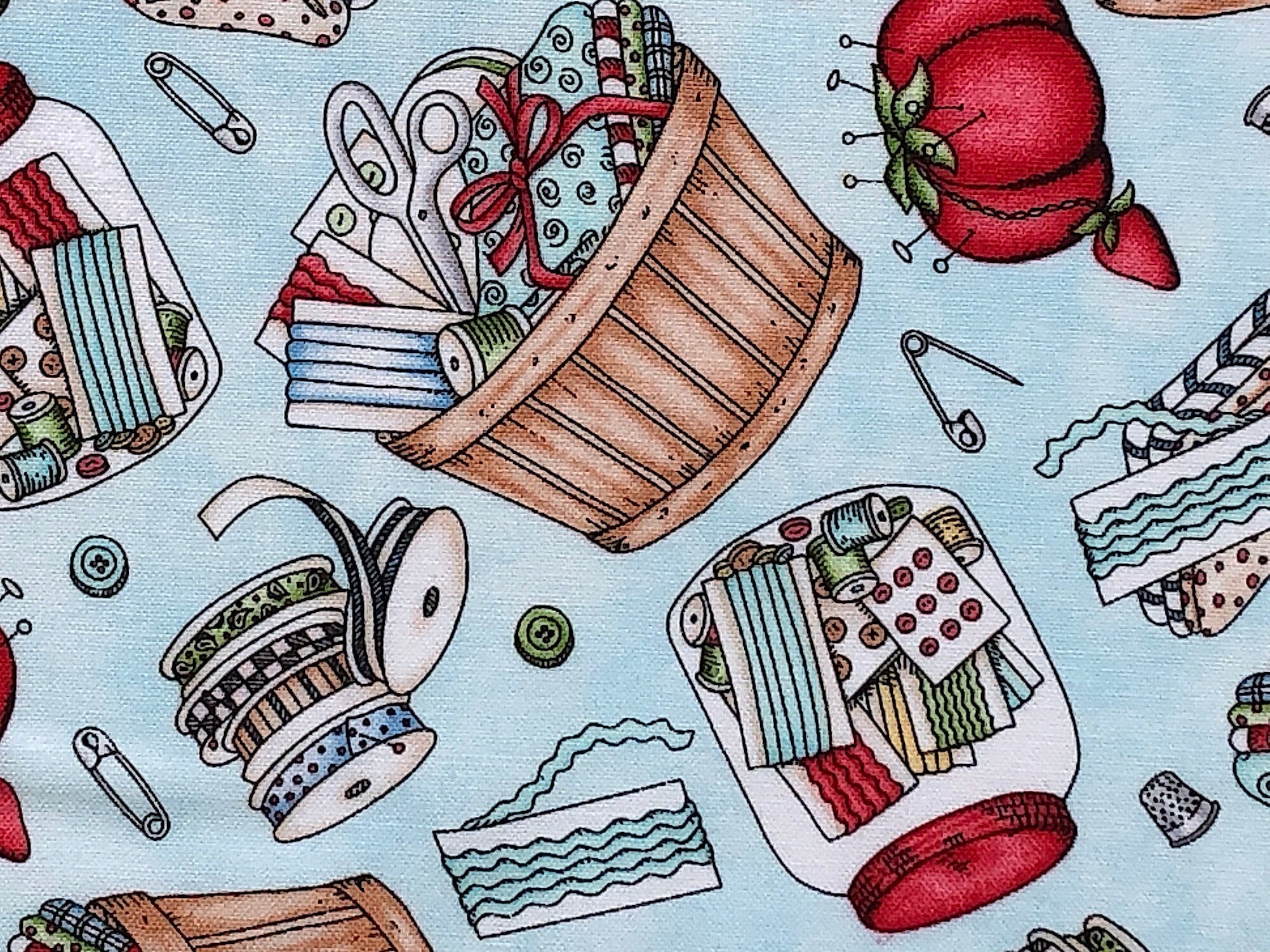 This fabric is covered with sewing notions such as buttons, thread, scissors, pincushions, fabric and more. There are also baskets and jars filled with sewing notions. 