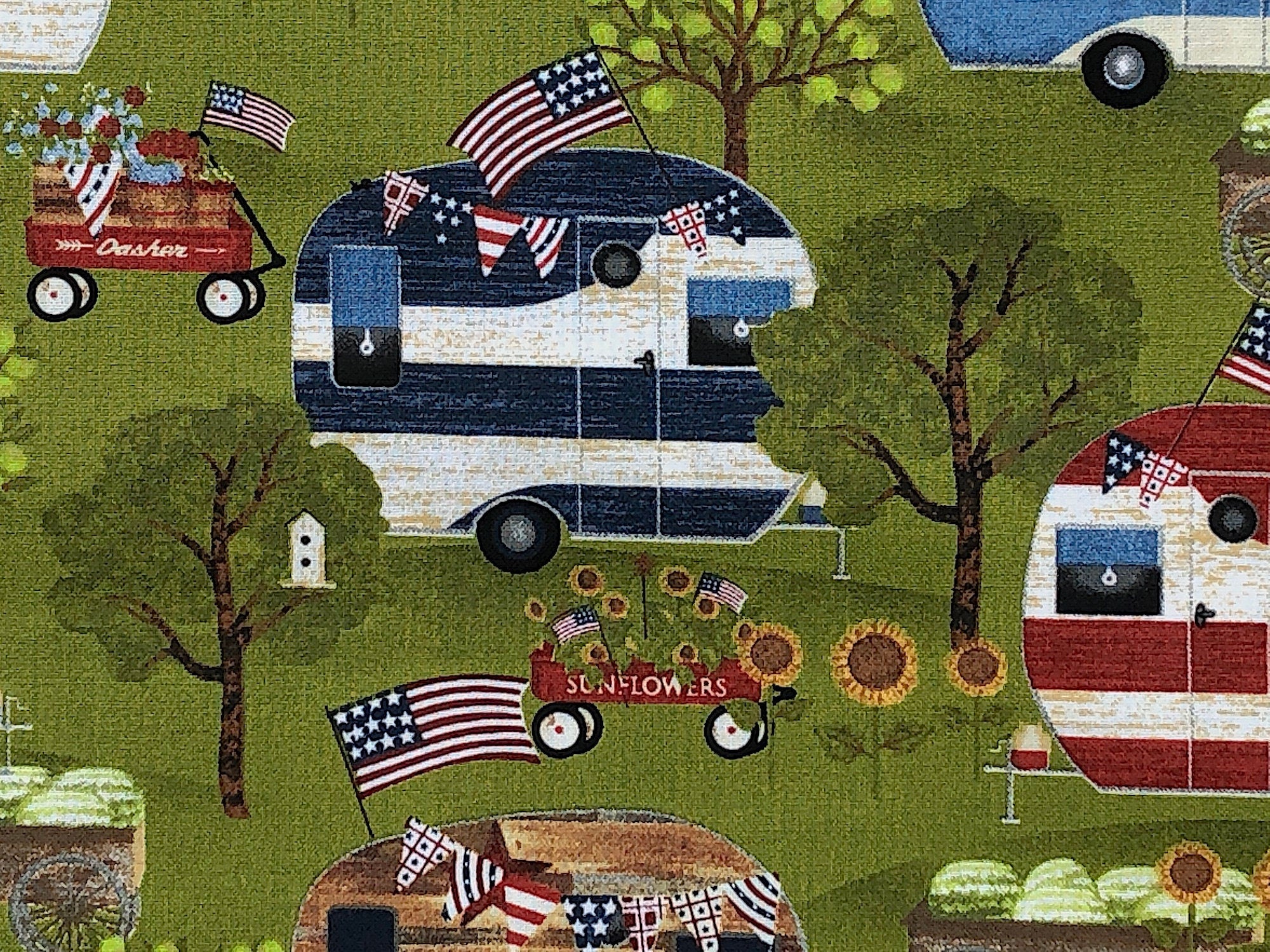 Close u of blue and white travel trailer, trees, USA Flag, sunflowers and more.