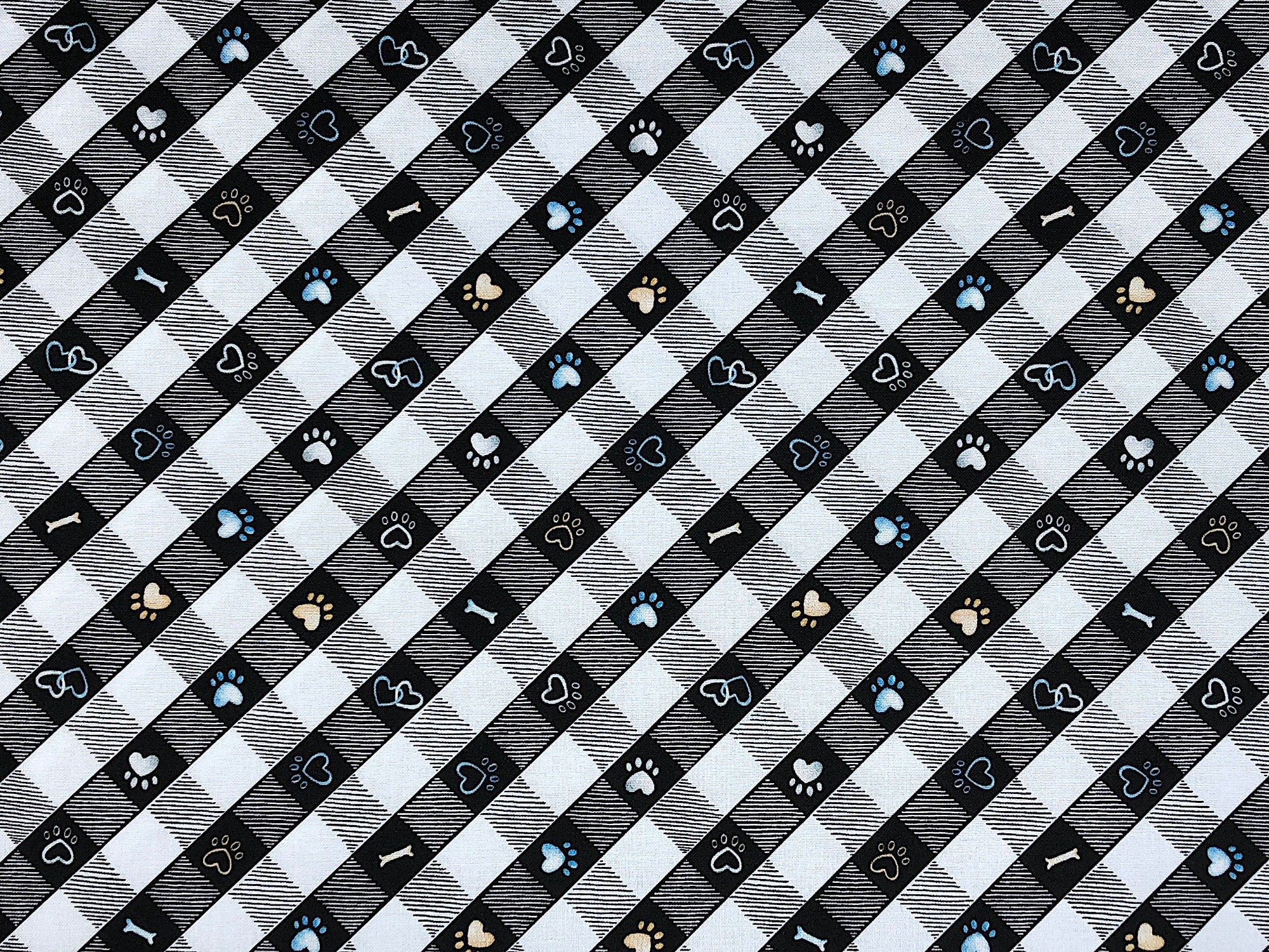 This black and white plaid fabric is covered with paw prints and dog bones. This fabric is part of the Think Pawsitive collection designed by Andi Metz.