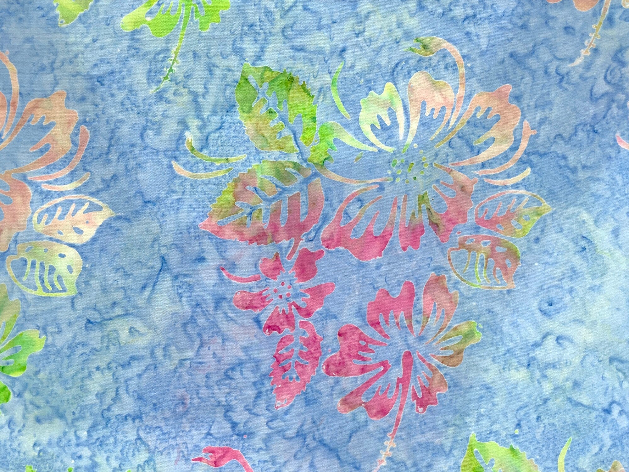Blue batik fabric covered with leaves and flowers.
