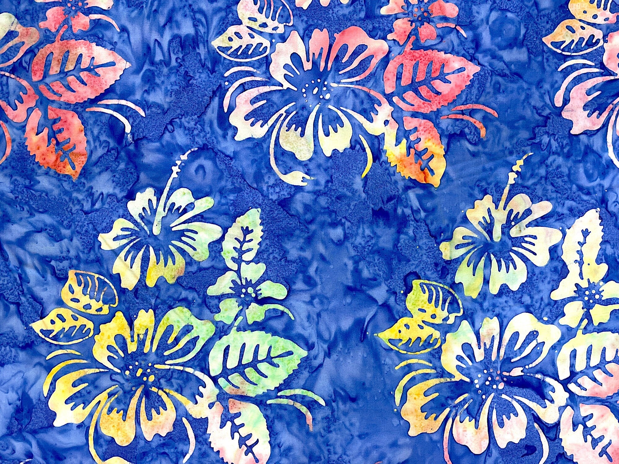 This fabric is covered with hibiscus. The flowers have shades of yellow, pink, blue and green. The background has shades of blue.