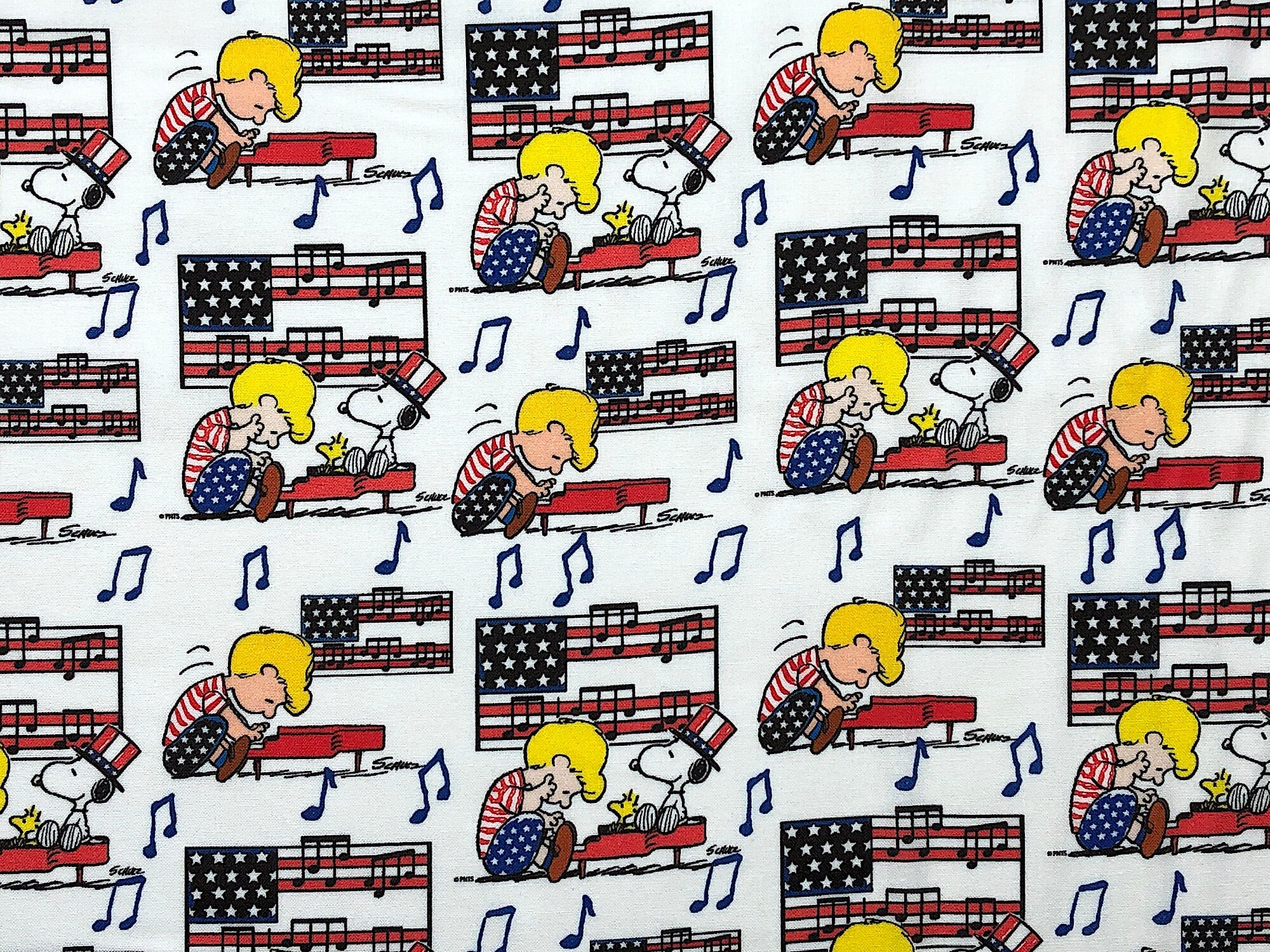 This fabric is called Linus Snoopy Americana and has Snoopy sitting on Linus piano. Linus is playing the piano and there are flags and music notes in the background of this white fabric.