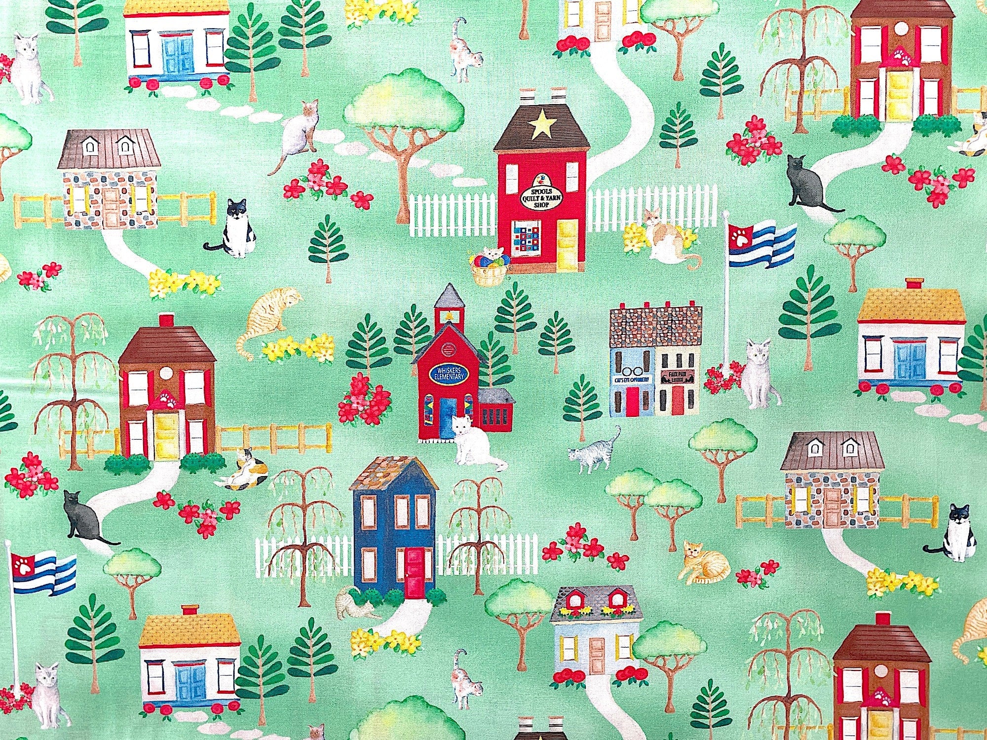 This green fabric is covered with buildings, cats, trees, flowers and more. 