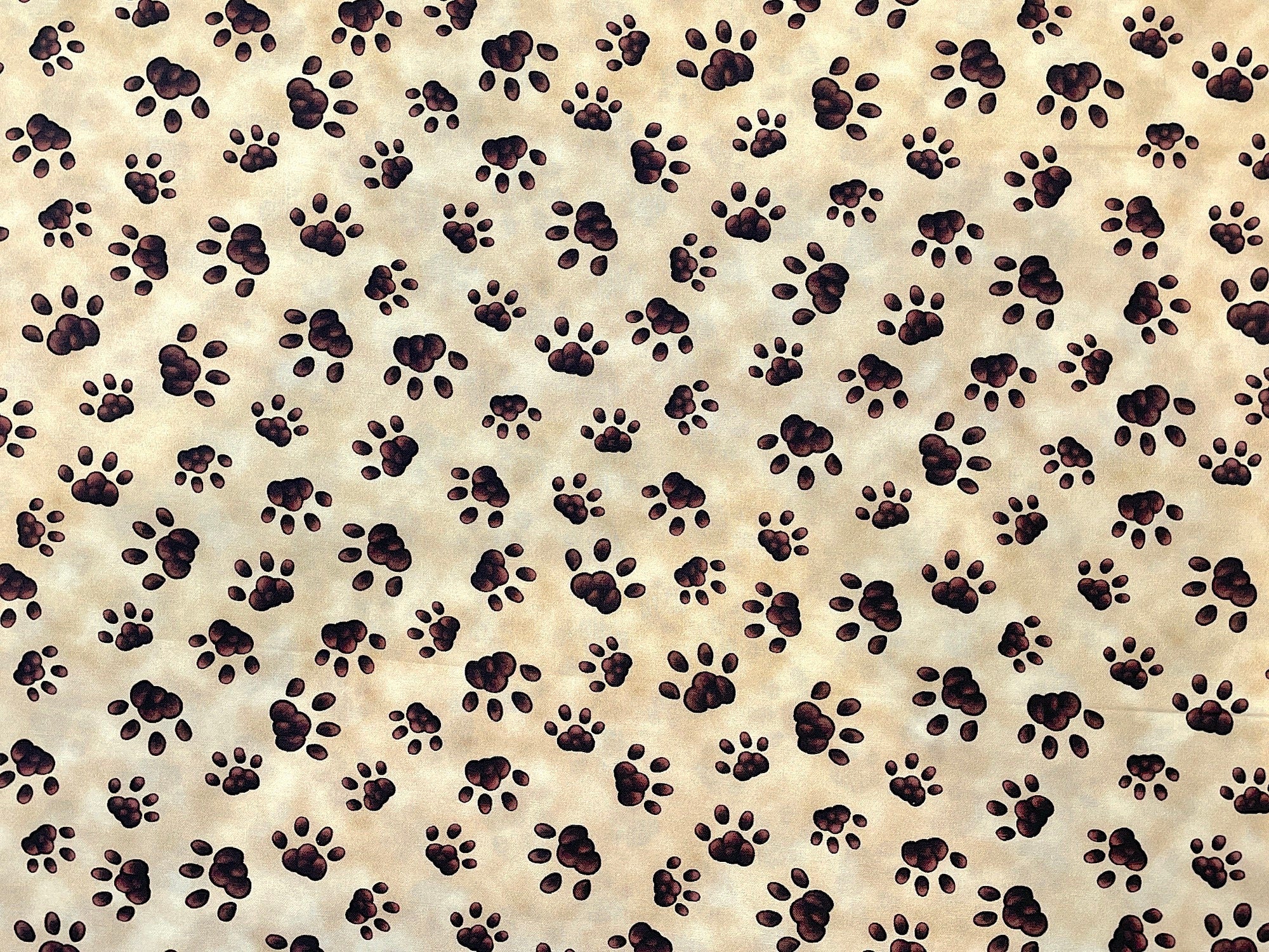 This cream colored cotton fabric is covered with shades of brown paw prints.
