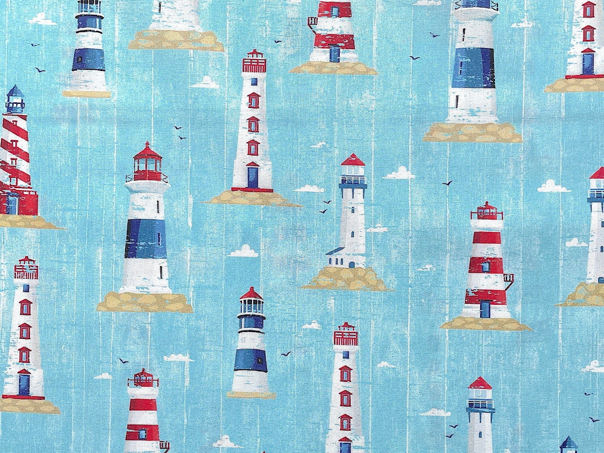 Light blue cotton fabric covered with red, white and blue light houses.
